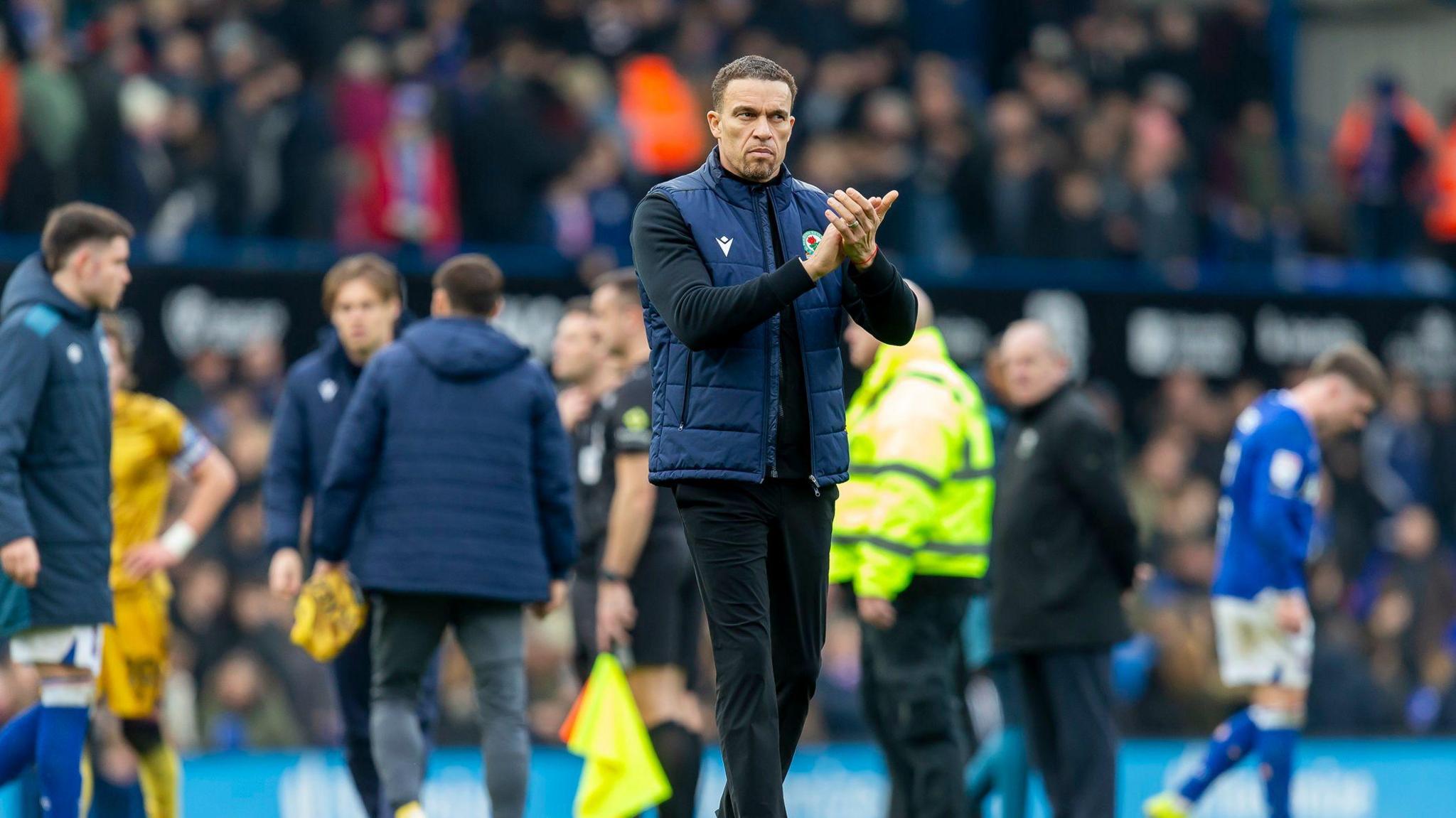 A photo of Valerien Ismael applauding fans in a blue gilet with black trousers at Portman Road