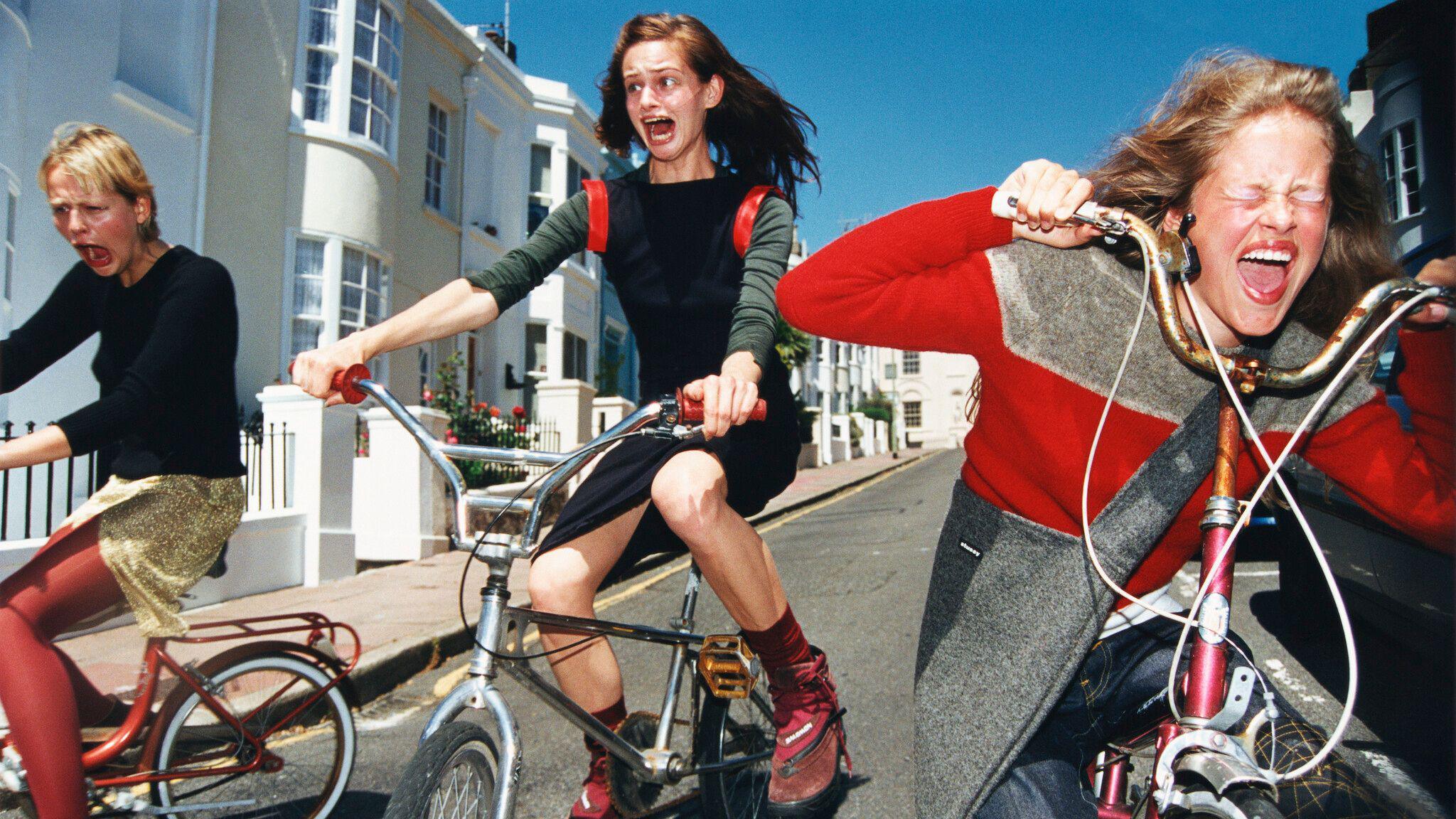 Girls wheel their bikes downhill whilst screaming - another image from the exhibition