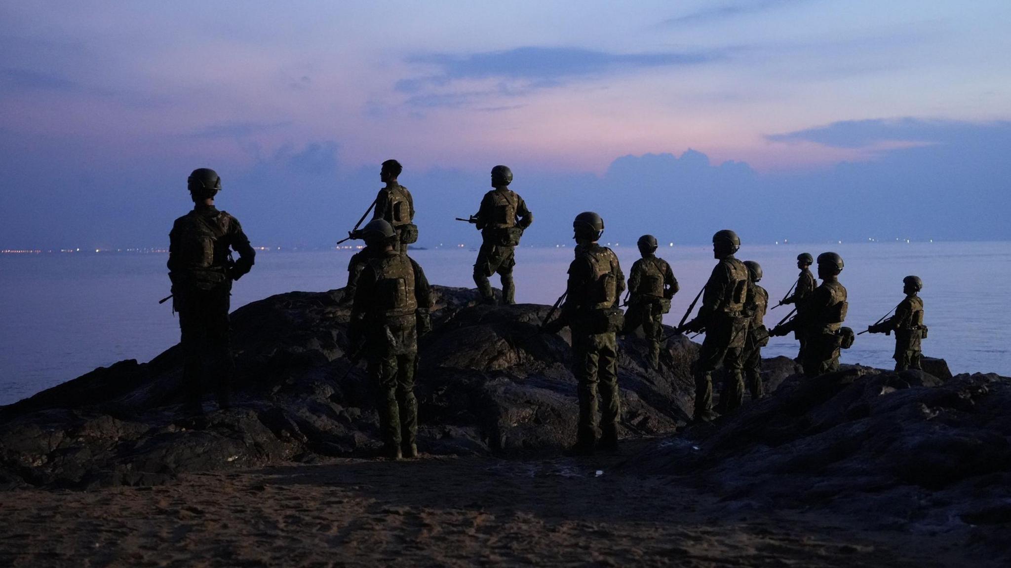 Taiwanese soldiers are seen at dusk or dawn, standing on the top of a piece of land, looking out at sea. 