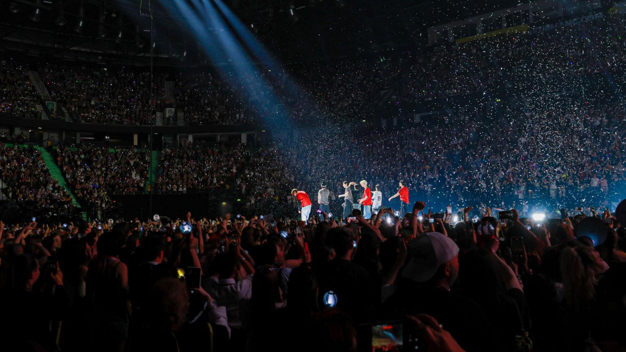 K-pop band ENHYPEN in the centre of the stage showing thousands of fans in the arena watching them.