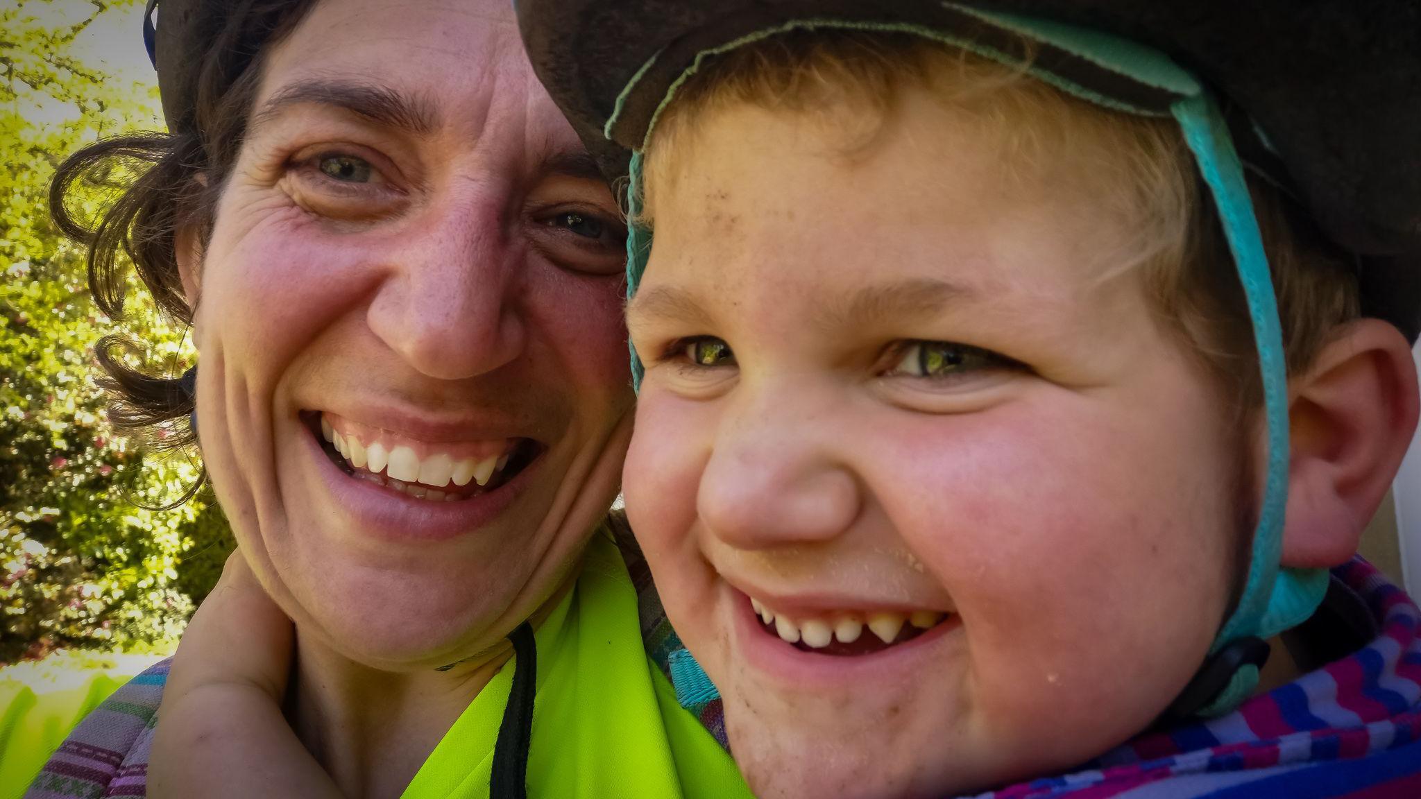 Ivor and his mum embrace for a selfie. both are smiling broadly and Ivor has his hand around mum's neck. They are wearing bike helmets and there is greenery in the background.