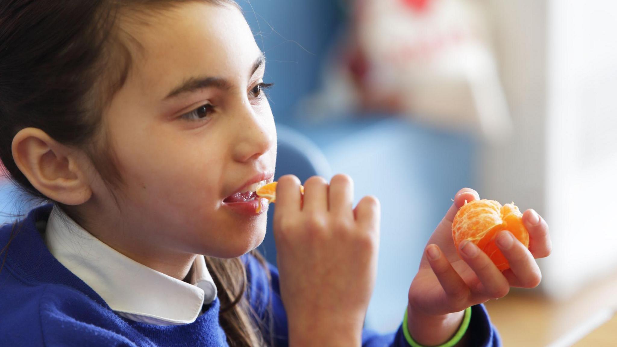 A girl eats a tangerine in her school uniform