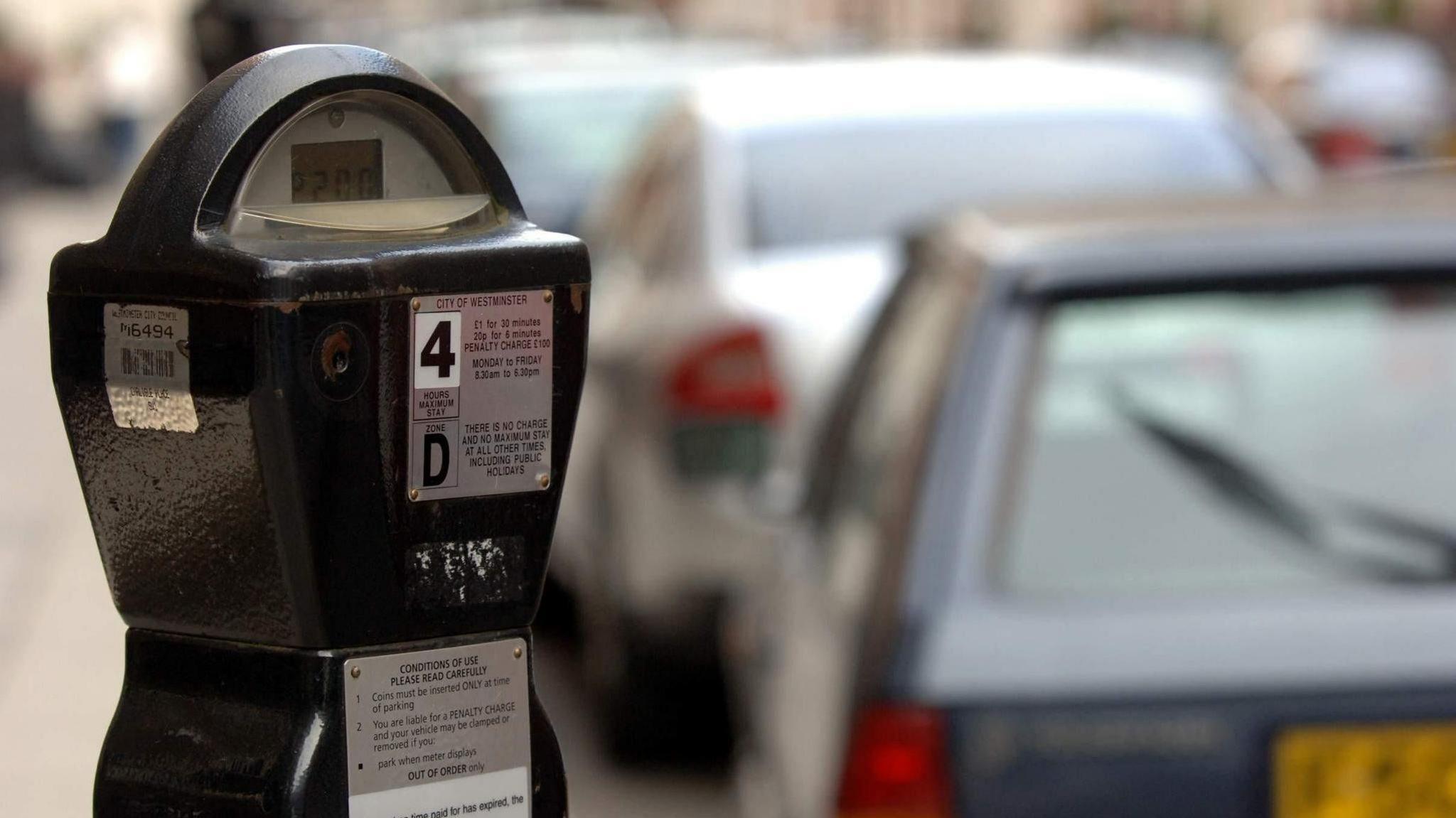 A parking meter is in focus with cars in a street blurred behind it.