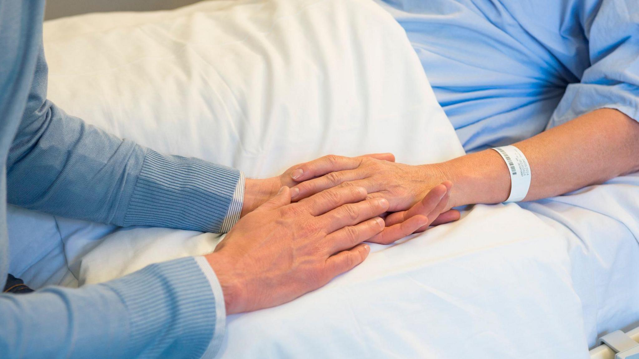 A man holds the hand of a woman lying in a hospital bed