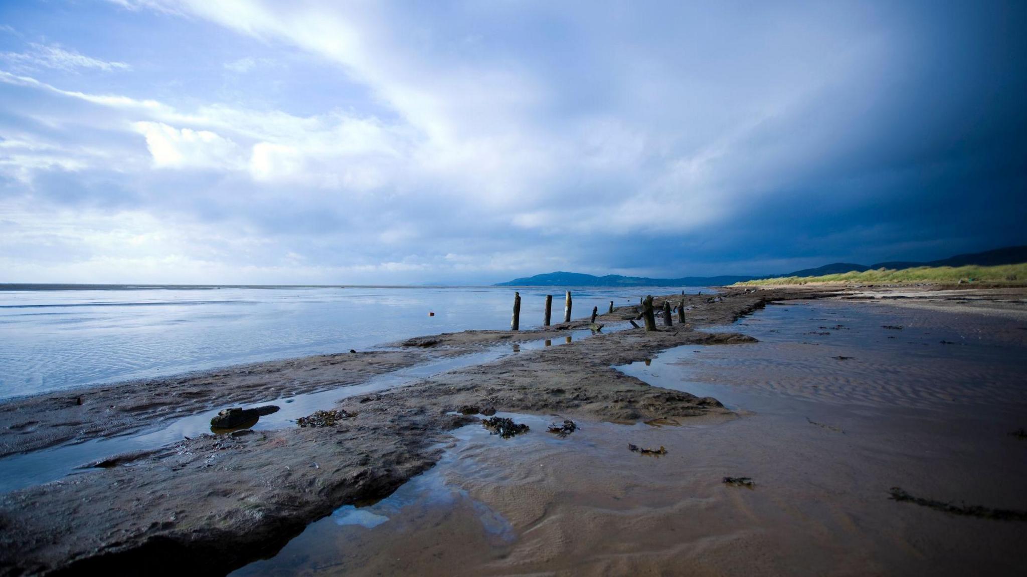Mudflats on the Solway coast in southern Scotland with water to the left and hills and grass to the right