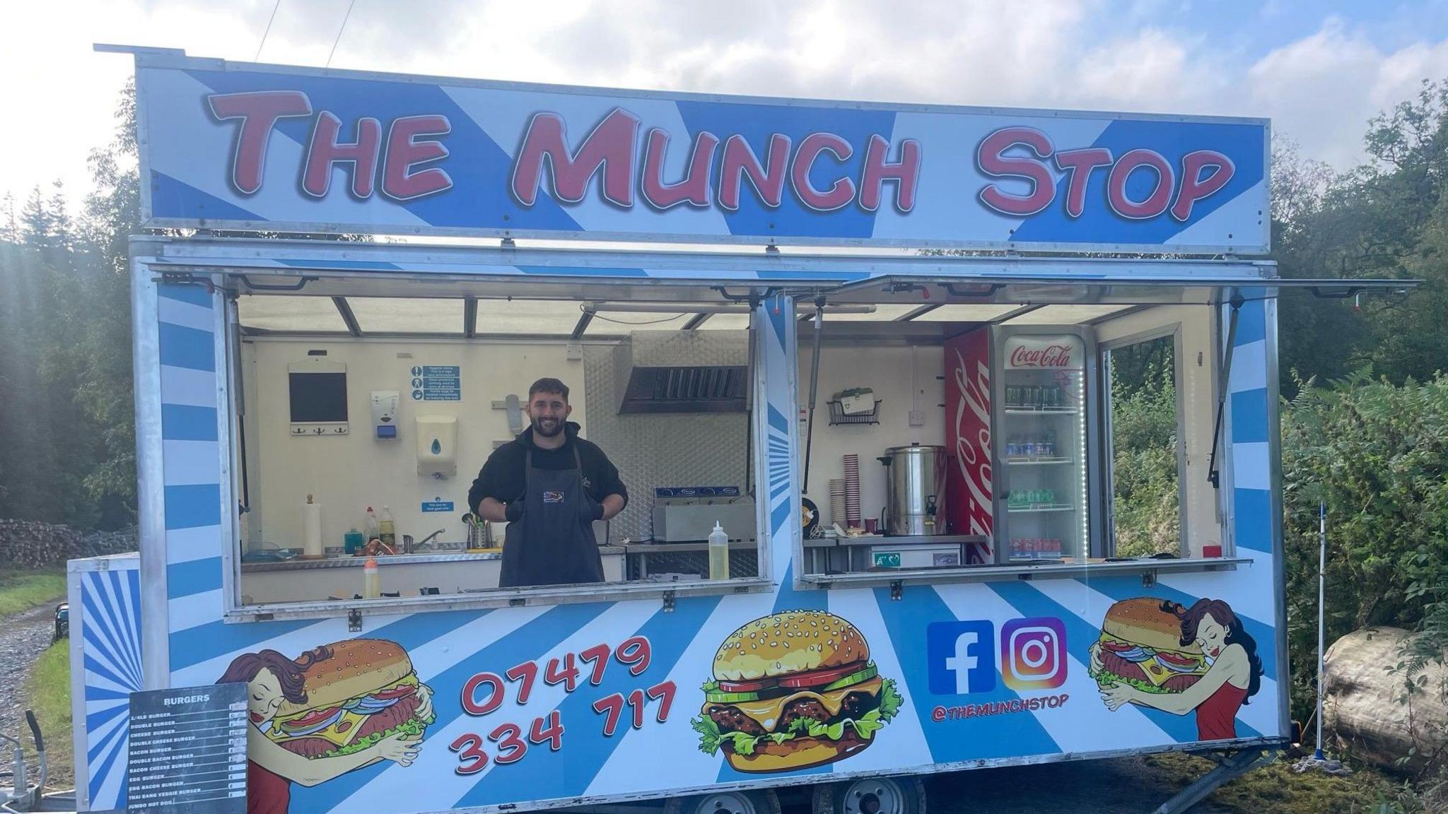 Picture of business owner Jordan Jones stood inside his blue and white striped burger van. 