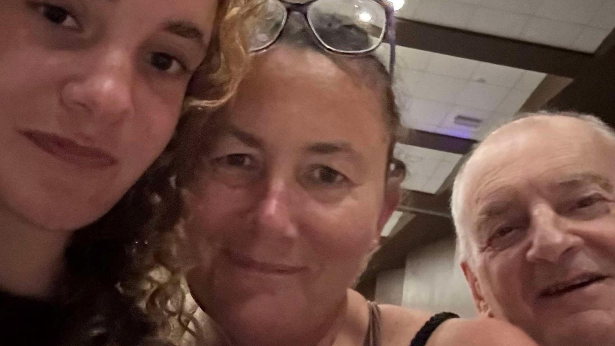 A young woman on the left is smiling, she has curly blonde hair. Next to her is a lady with her hair tied back, also smiling, and on the right is a man who is also smiling. The picture is selfie-style and they're all looking directly into the camera.