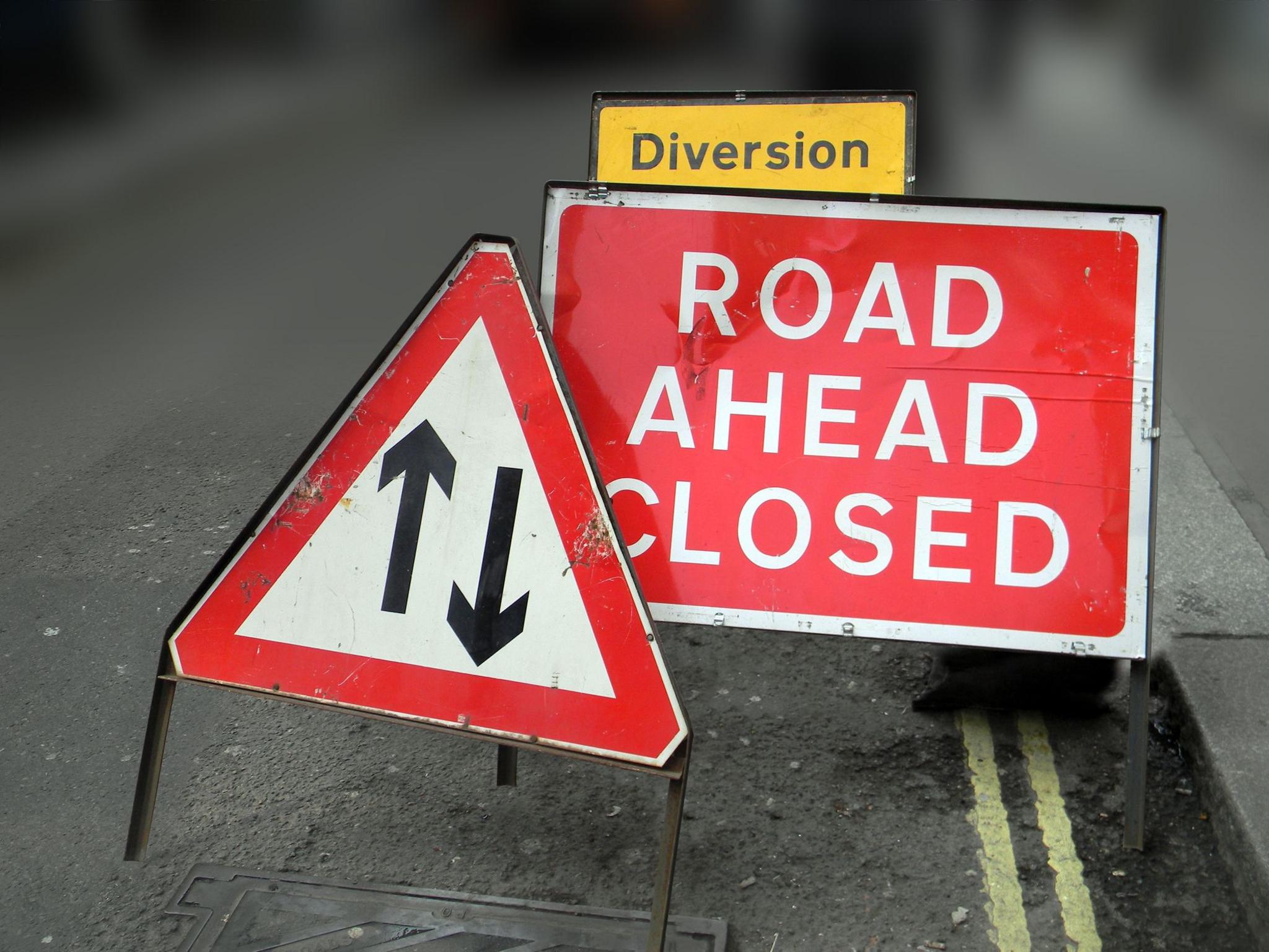 Three red, white and yellow road closure signs on a road.