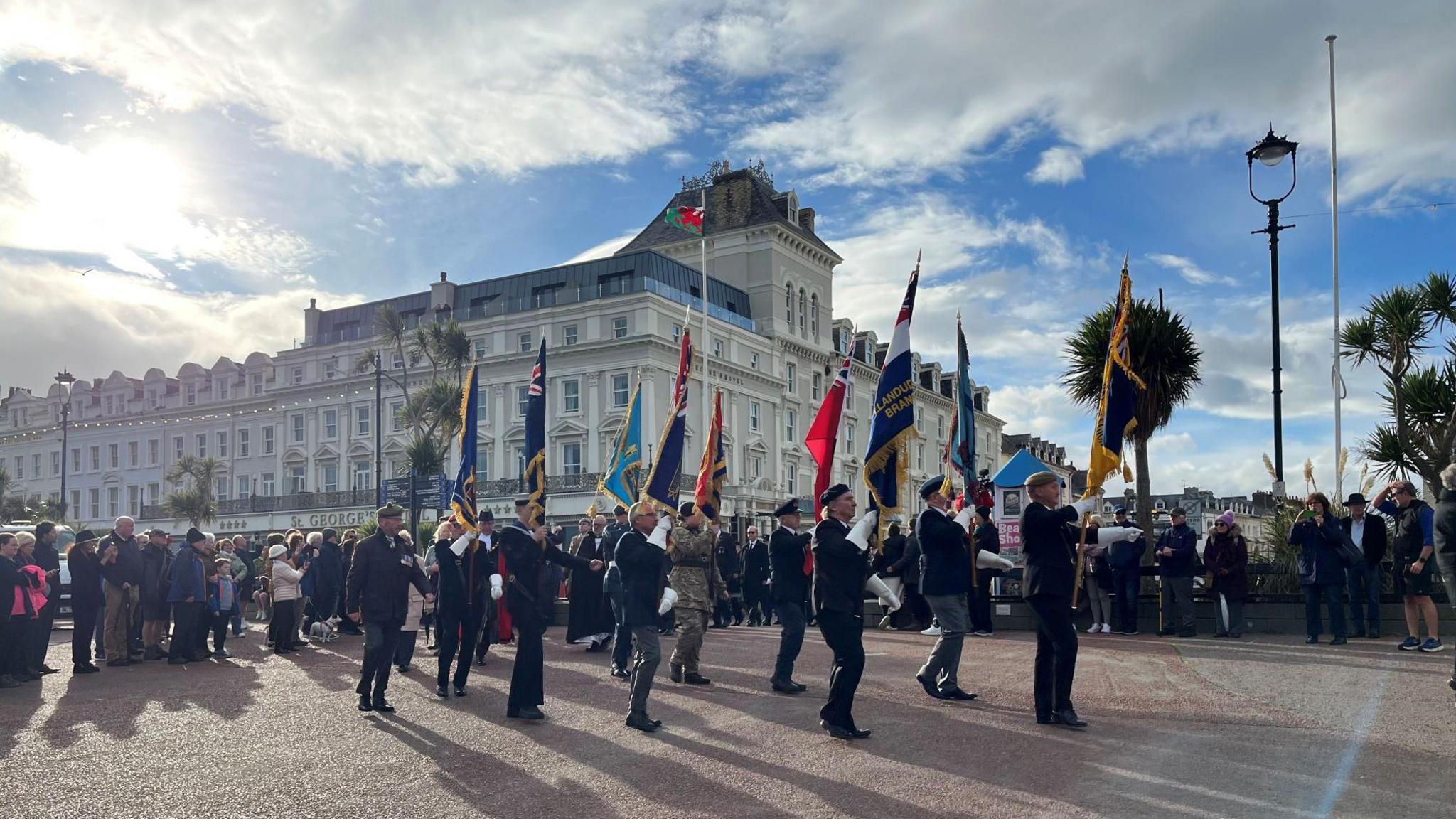 Photograph showing a group of men from the armed forces holding flags during a ceremony in Llandudno.