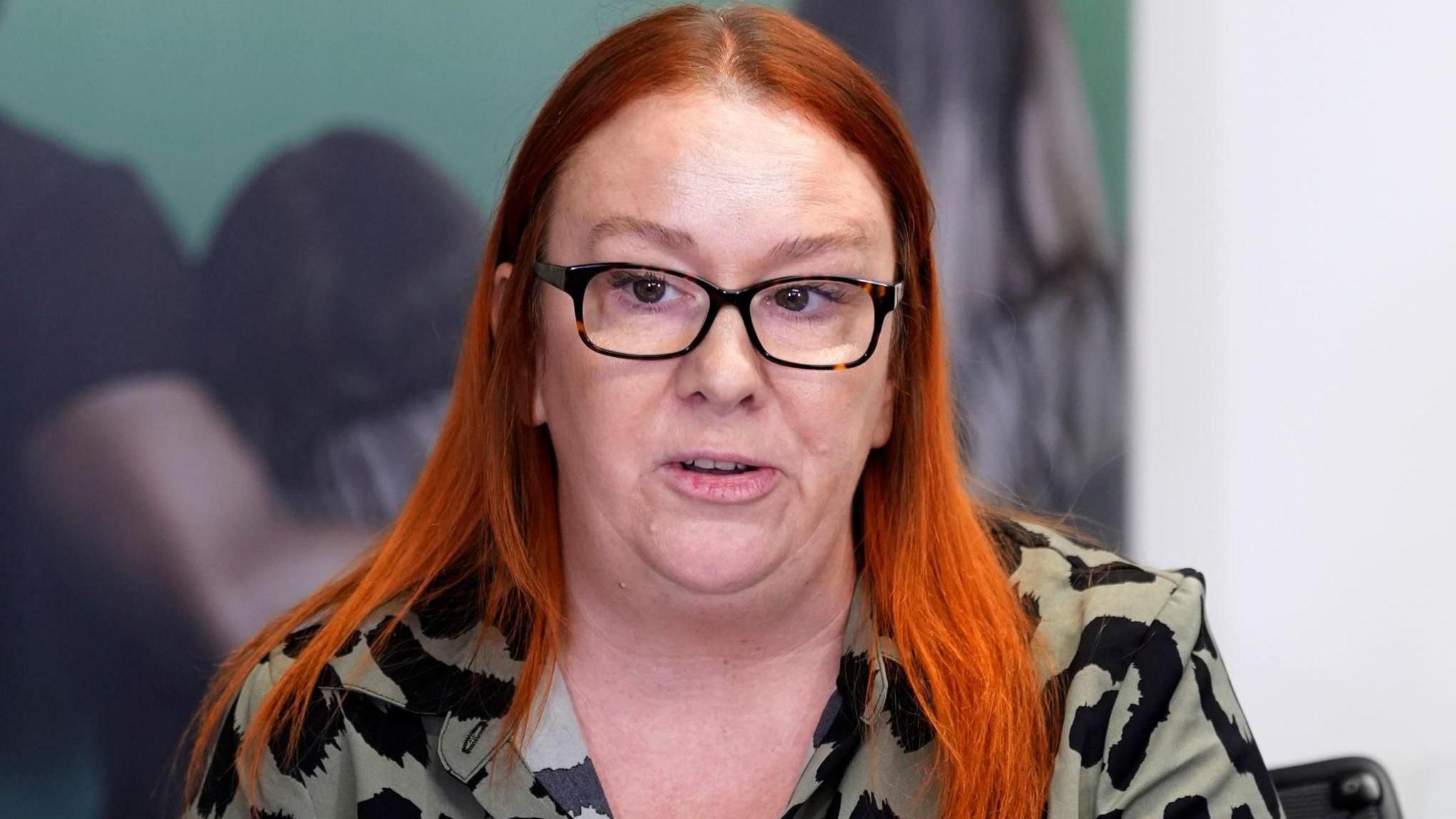 Grua me flokë të kuq dhe këmishë kaki dhe të zezë - mban syze me kornizë të errët