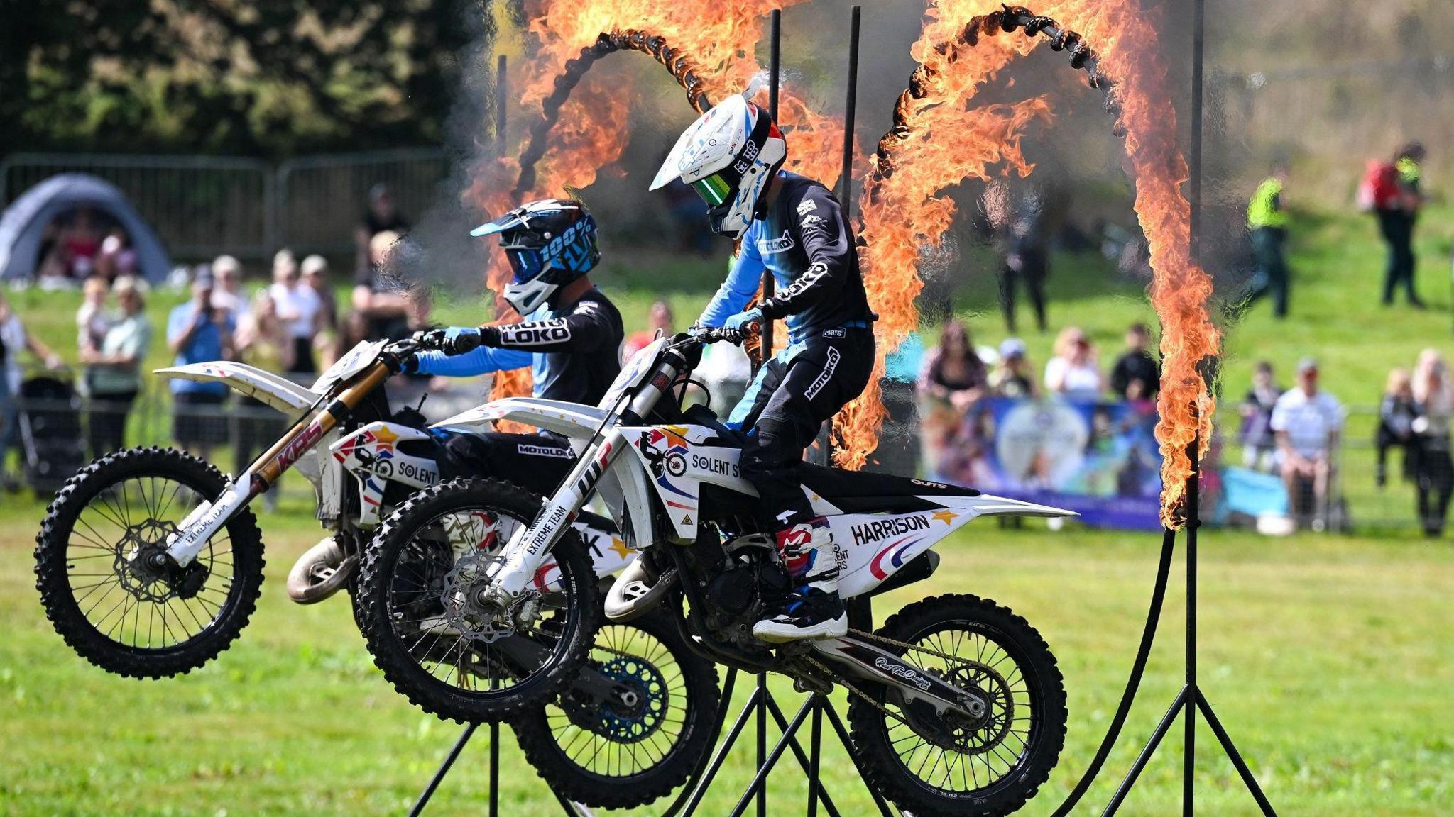 Two motorcyclist past through fiery hoops as crowds watch on in the background at the Bristol Balloon Fiesta