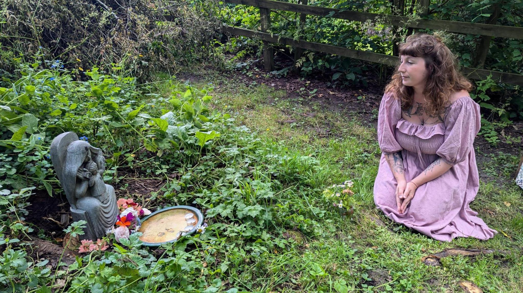 Jenny Henry is kneeling on the down looking at the mother and child sculpture in its new location