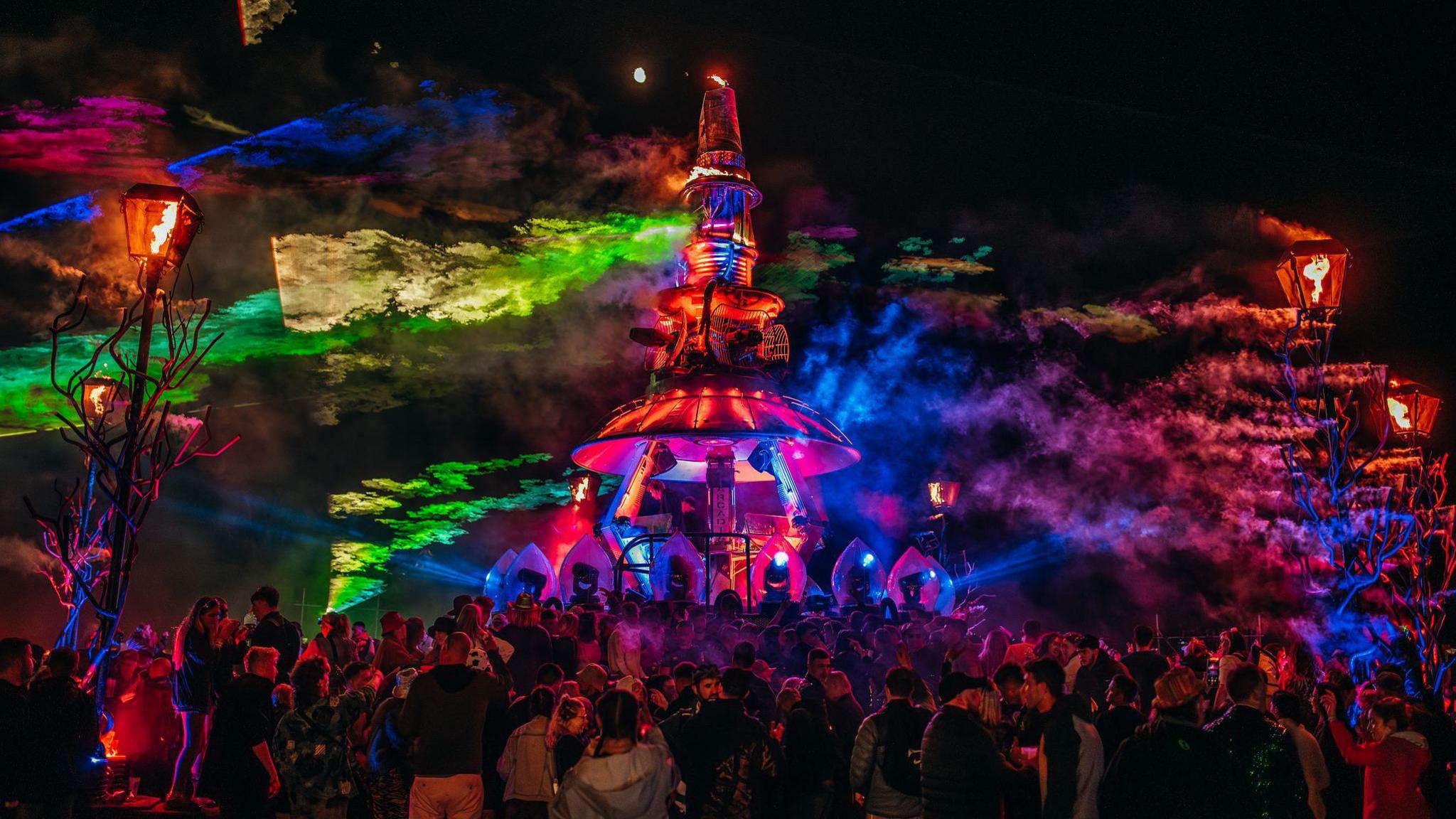 A crowd stand around the Arcadia attraction with colourful beams of light around it