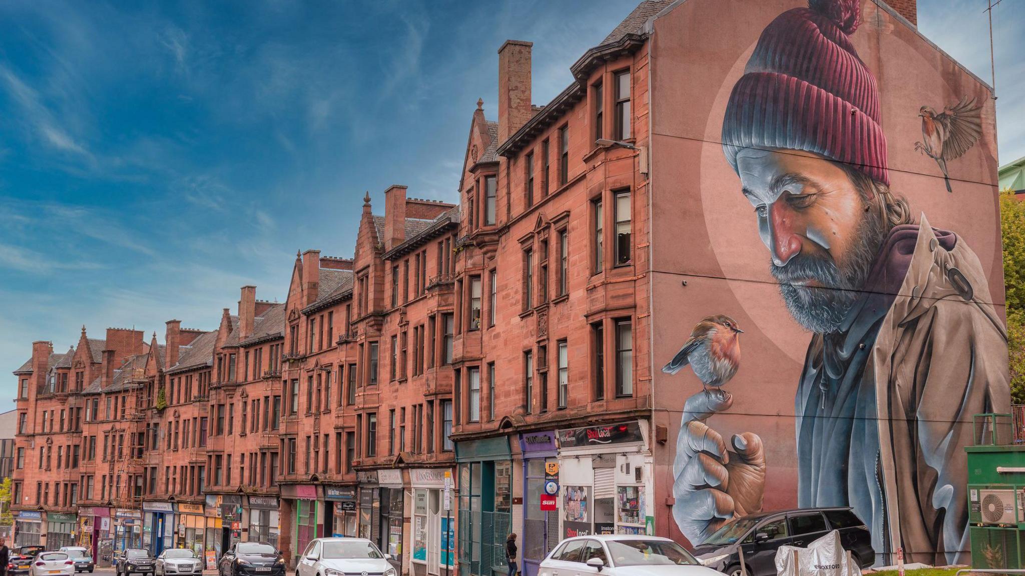 A mural by the Australian artist Smug (Sam Bates) on a gable end of a tenement block in Glasgow's High Street depicting a modern interpretation of the city's saint, St Mungo, saving a robin.