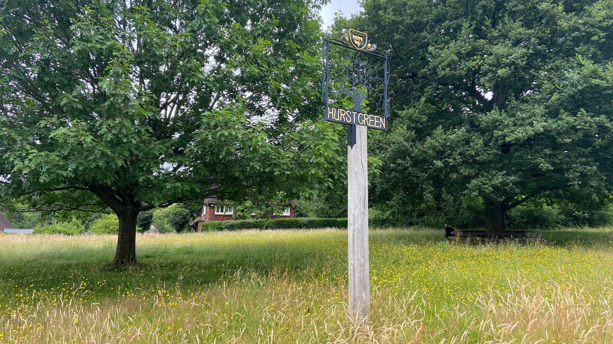 A metal and wood sign saying Hurst Green