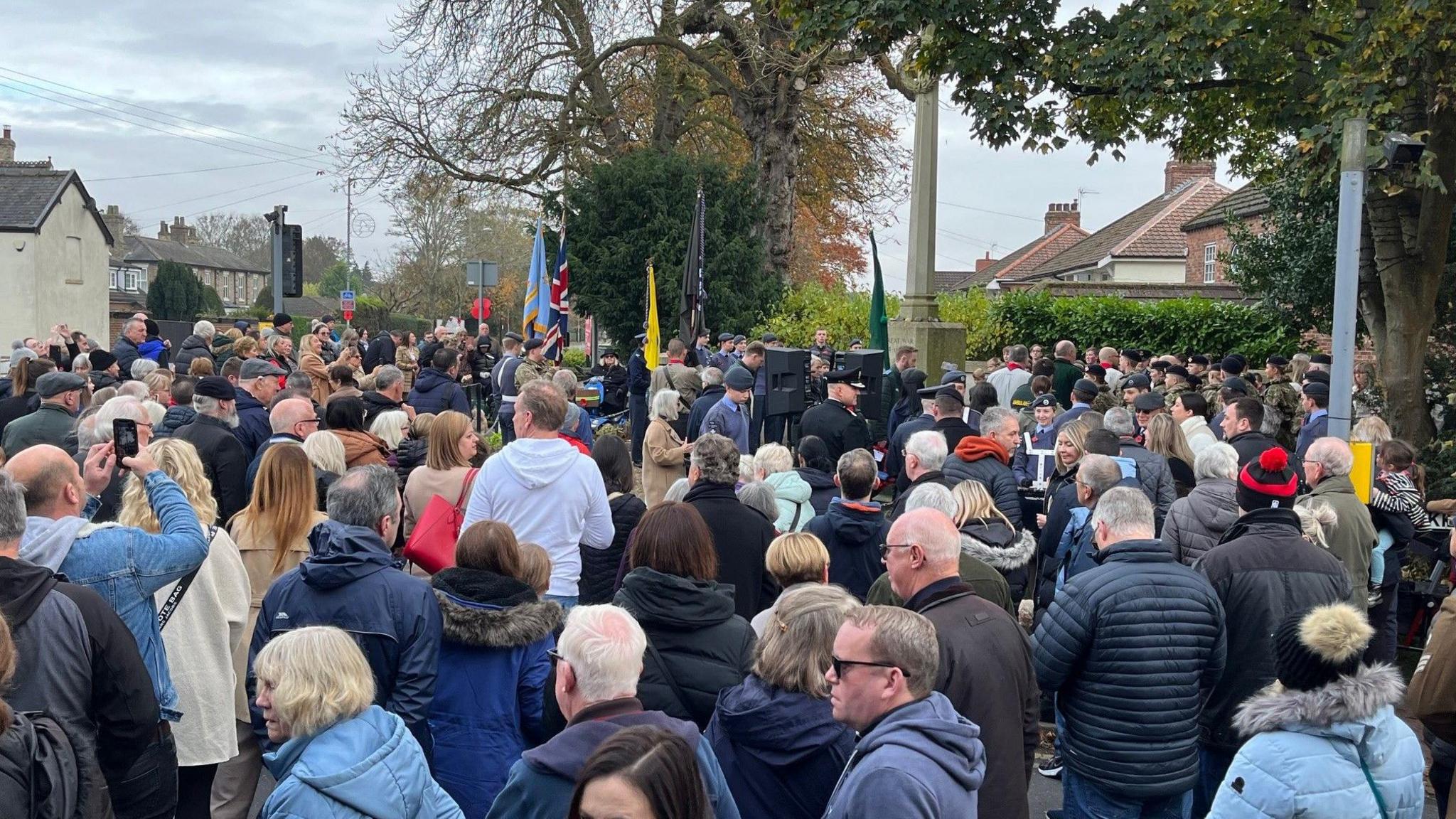 People in coats stand around in the cold to mark the event at the memorial at Brough