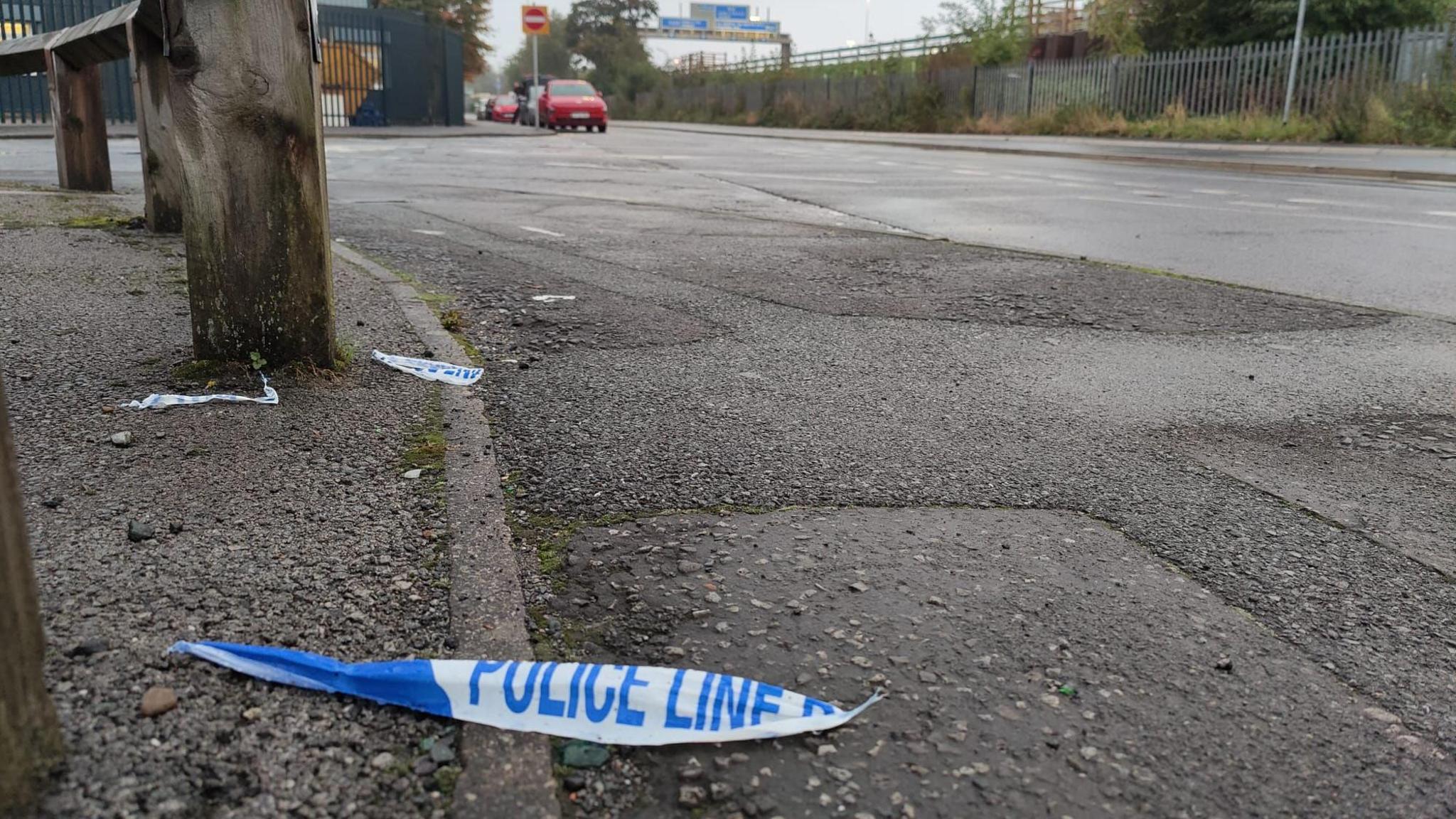 A piece of blue and white police line tape lies at the side of a road