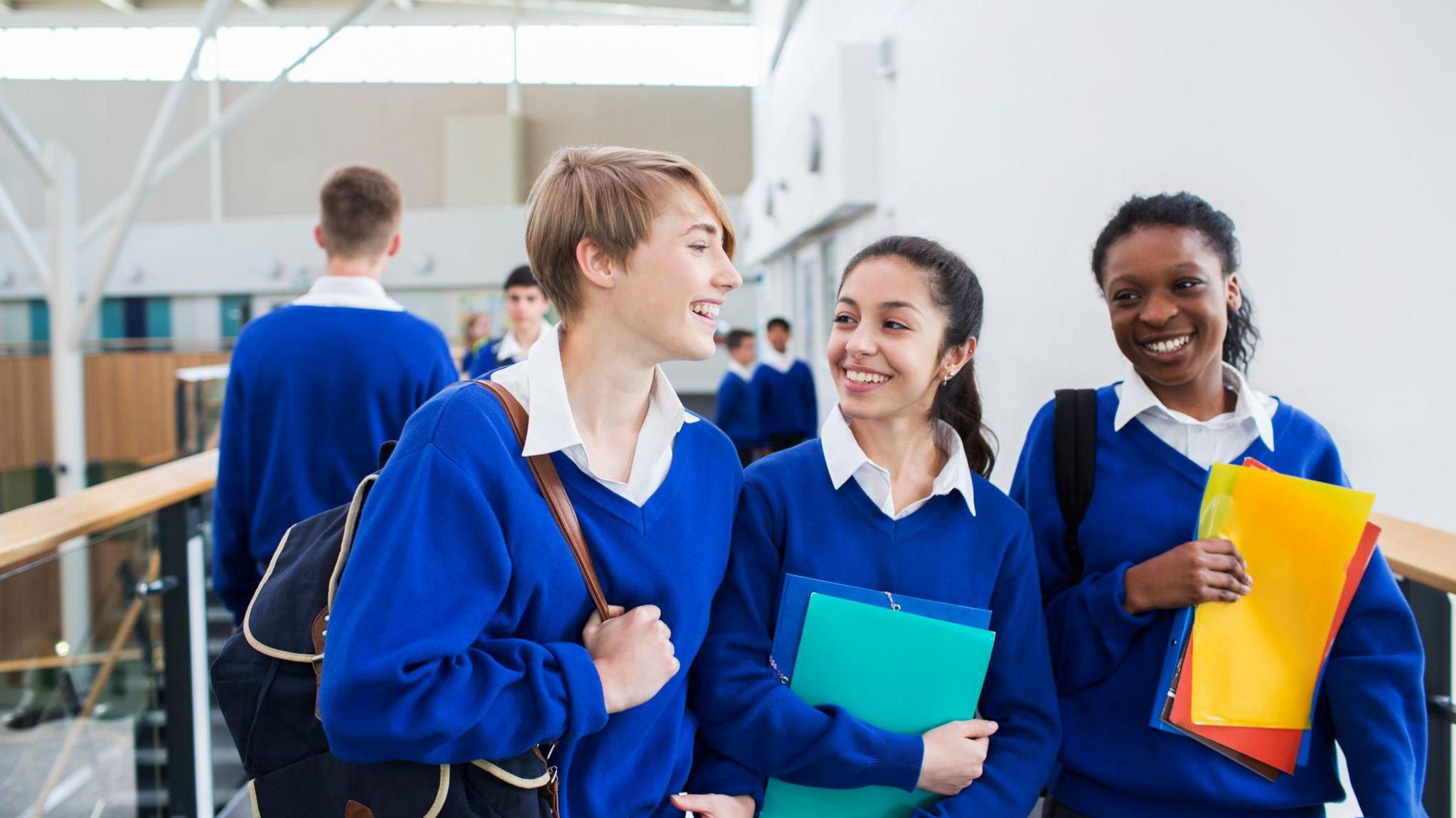 Smiling female students wearing school uniforms walking through school corridor