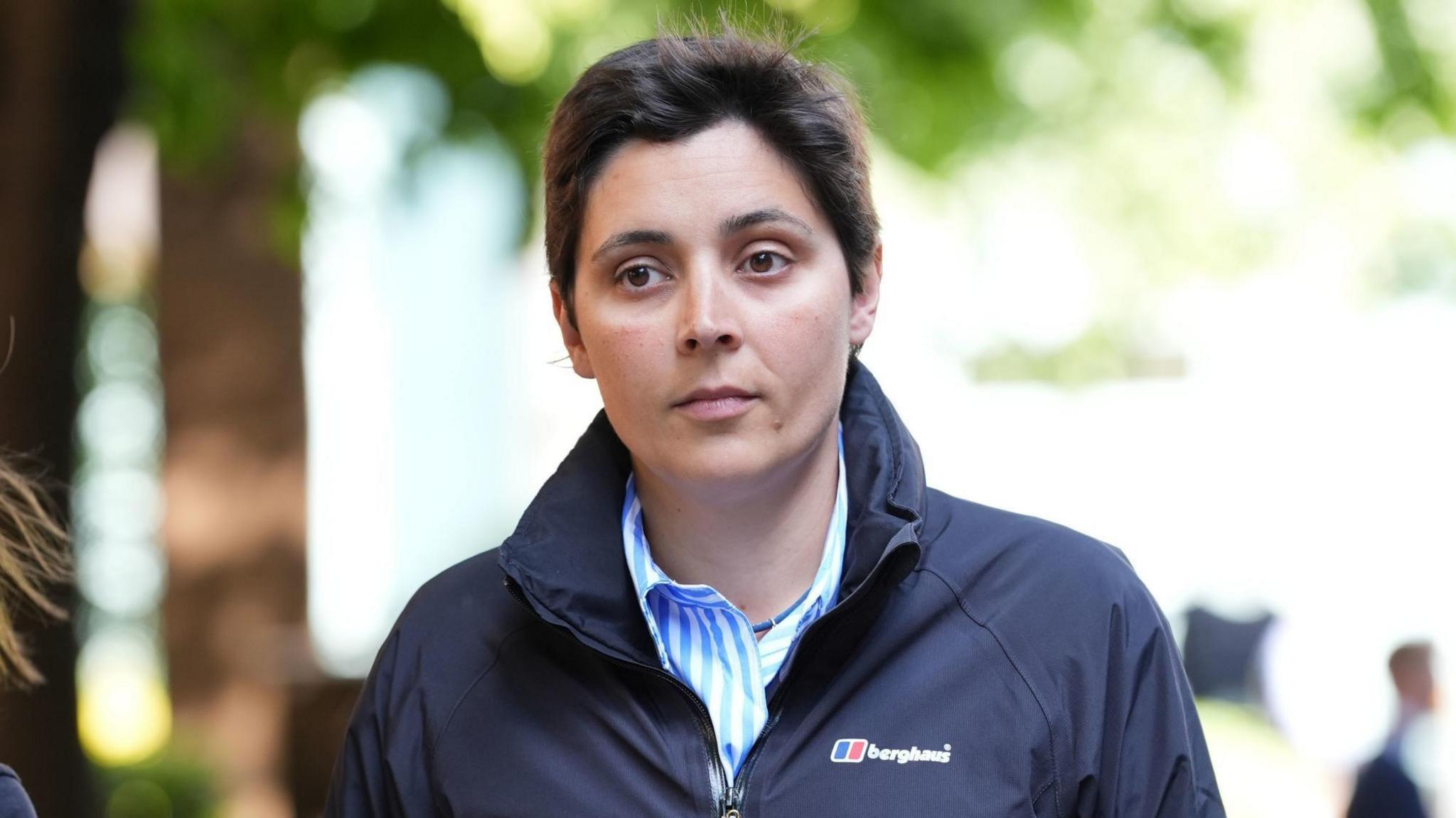 A woman with short hair wearing a dark, plain Berghaus jacket and a blue and white striped shirt with a collar.