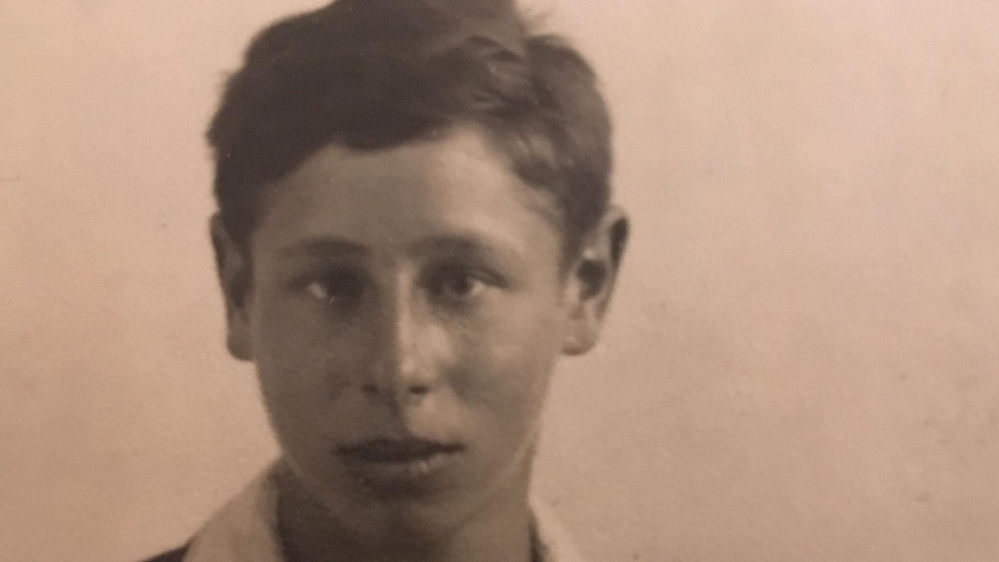 An old sepia photo shows a teenage boy wearing a dark jumper and a white shirt.