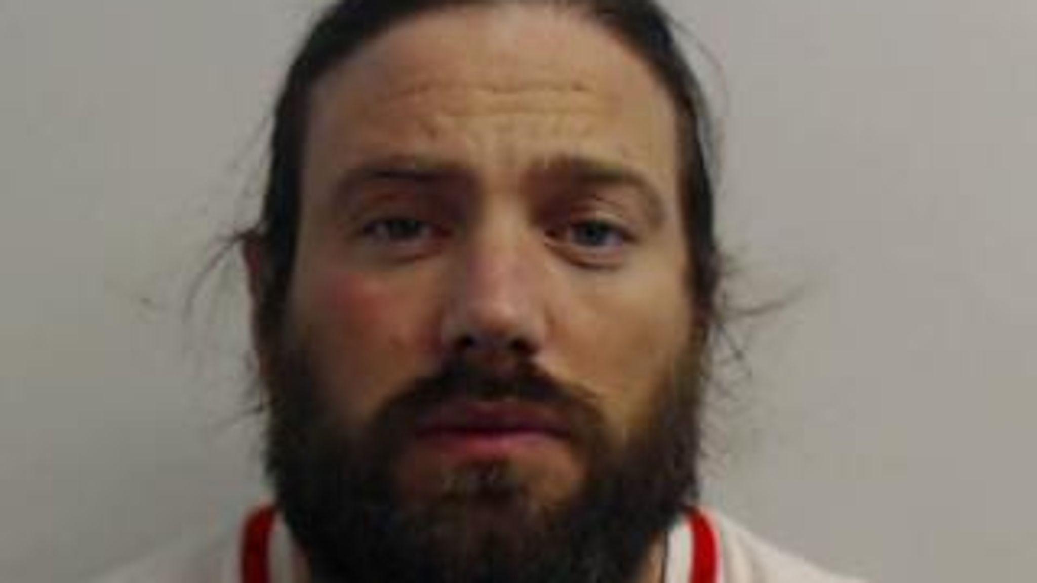 Mugshot of Harkins. He looks straight at the camera. He has long hair, tied back, and a beard. He looks dishevelled.