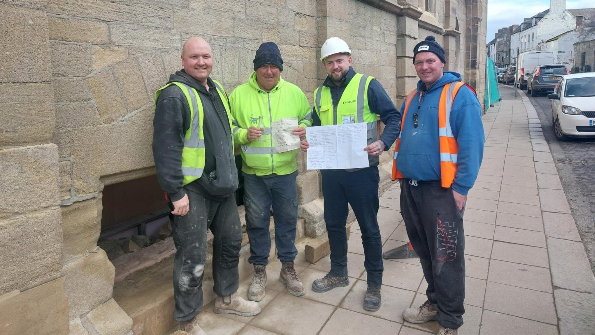 Four crew members in high-vis jackets standing outside wall cavity where message in bottle was found. Anthony Gibbons, second from right, is wearing a white helmet as well. 