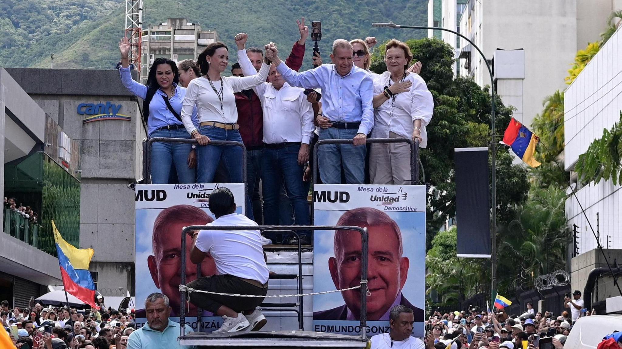 Opposition leader Maria Corina Machado stands on a crowded open top bus with her supporters as it weaves through a huge crowd.