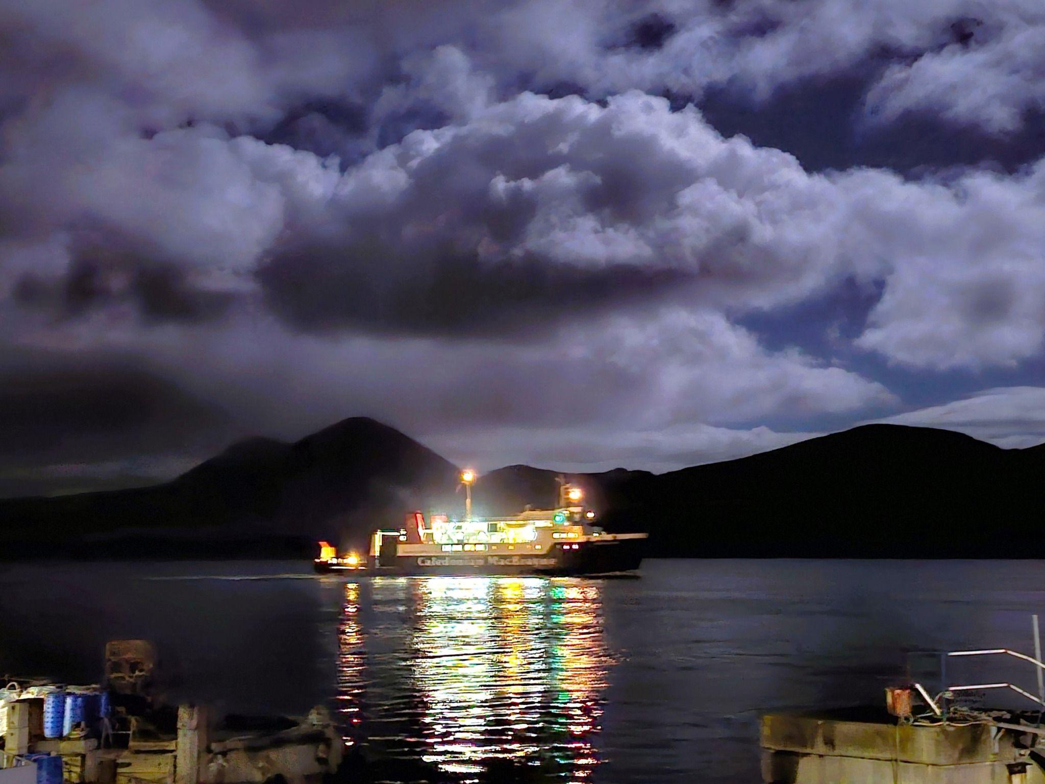 A brightly lit ship with a jetty in the foreground and the purple clouds in the moonlight