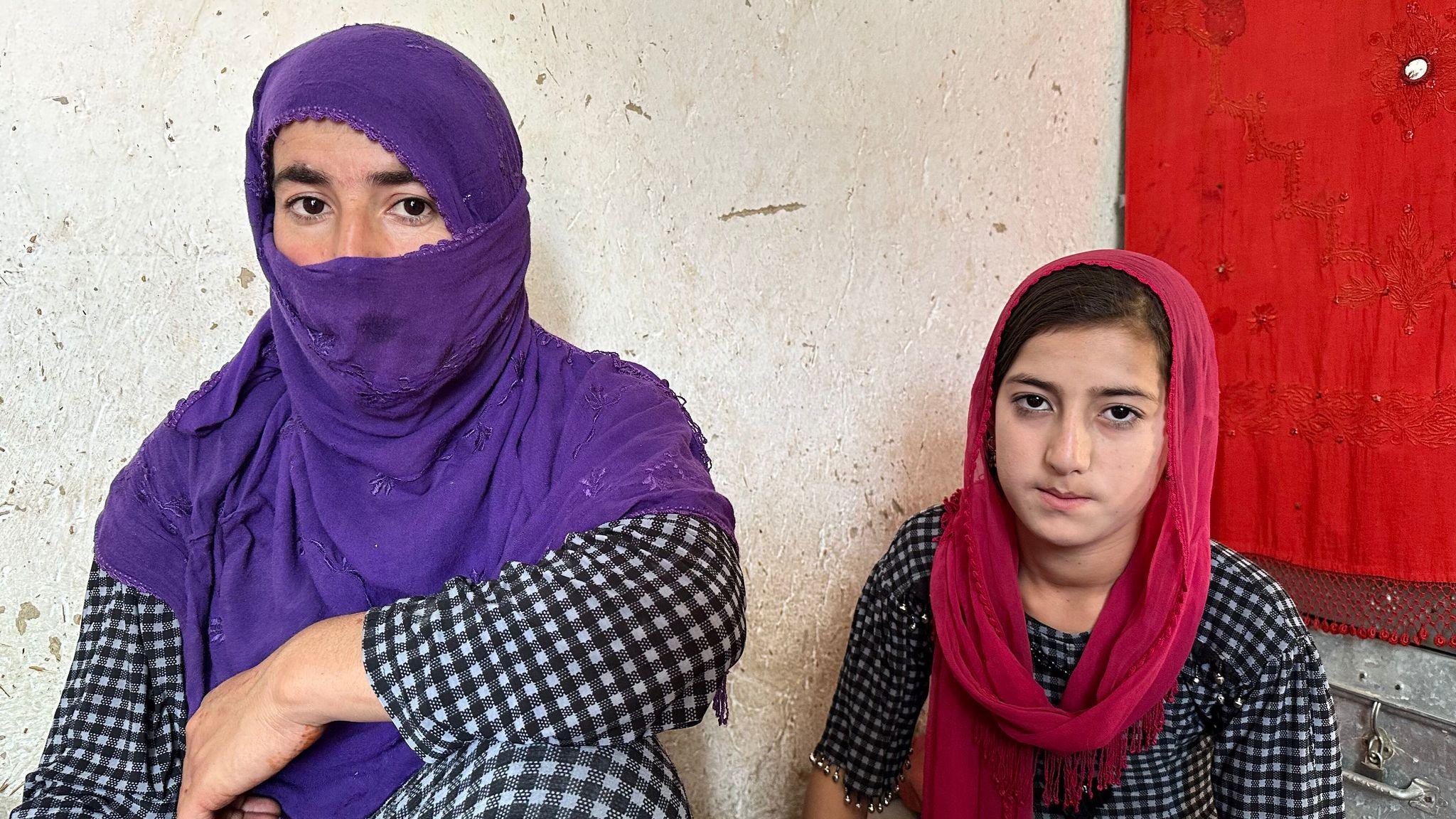 Bahisa and her daughter wear head scarves while looking at the camera as they're pictured at home against a wall and window with a red curtain.