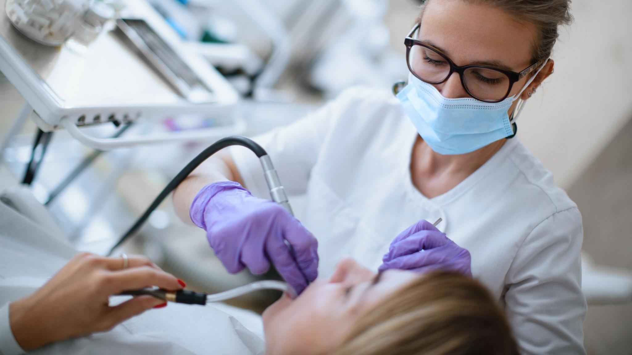 Dentist with facemask and purple gloves examining a patient's mouth