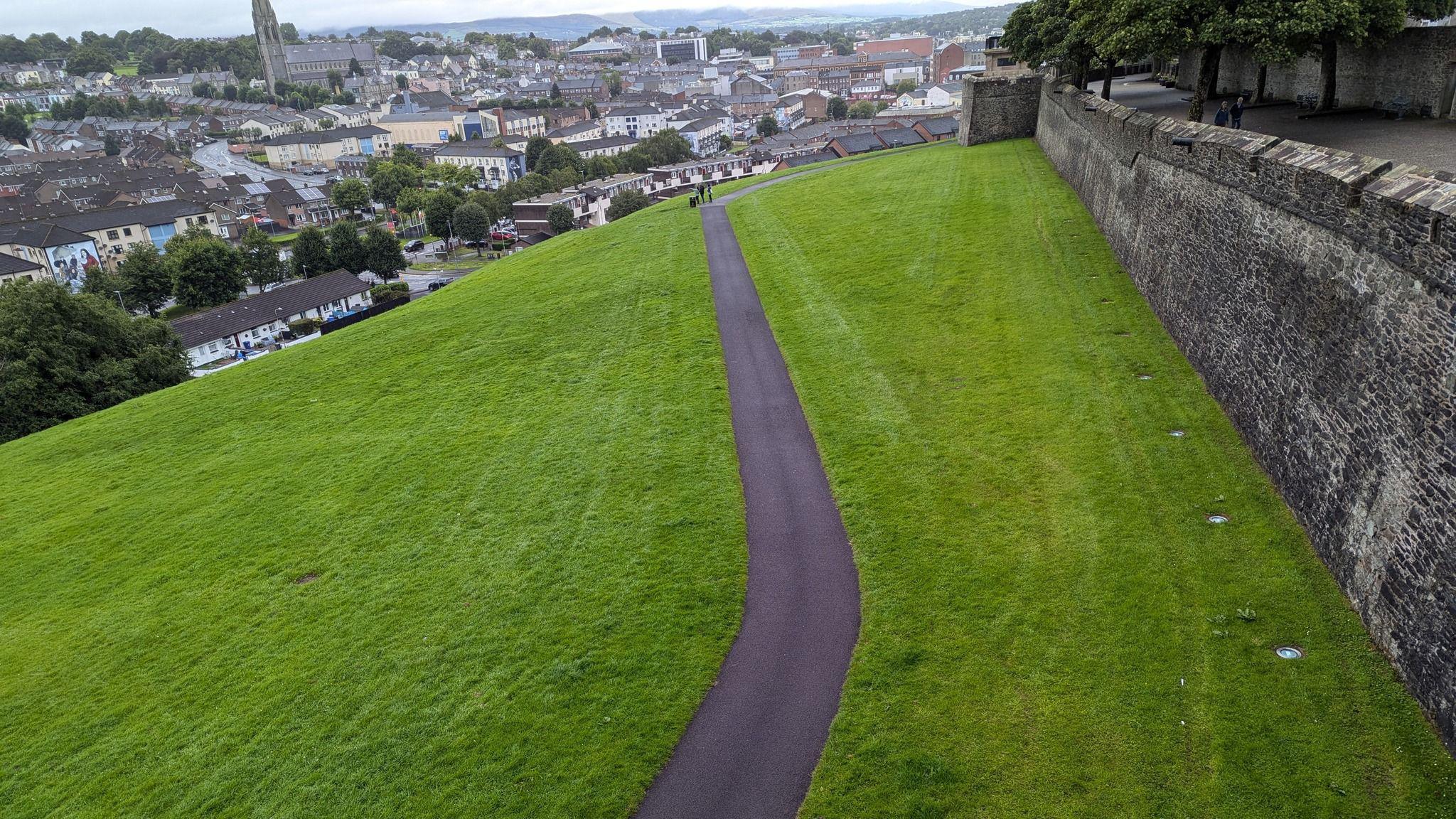 A grass bank in Derry that slopes from the city's wall on the right to the houses in the bogside area on the left