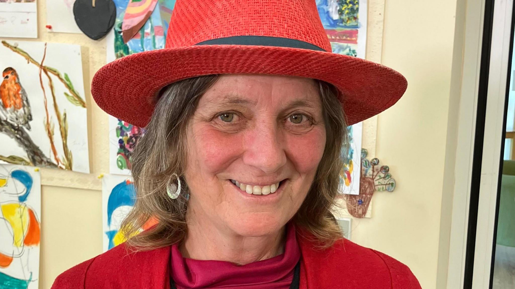 Joy Roodenburg-Vermaat. She is wearing a red straw hat which has hair sewn in. Joy is looking directly at the camera and smiling. 