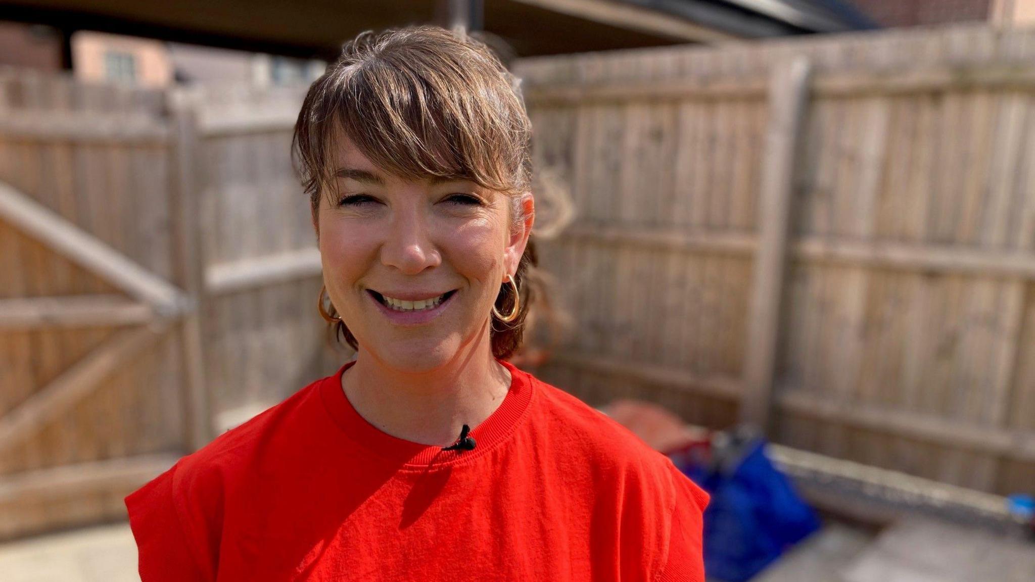 Bethan Davies o ymgyrch Cymru yn Ailgylchu.  Mae'n sefyll o flaen nifer o fagiau ailgylchu mewn gardd gefn.