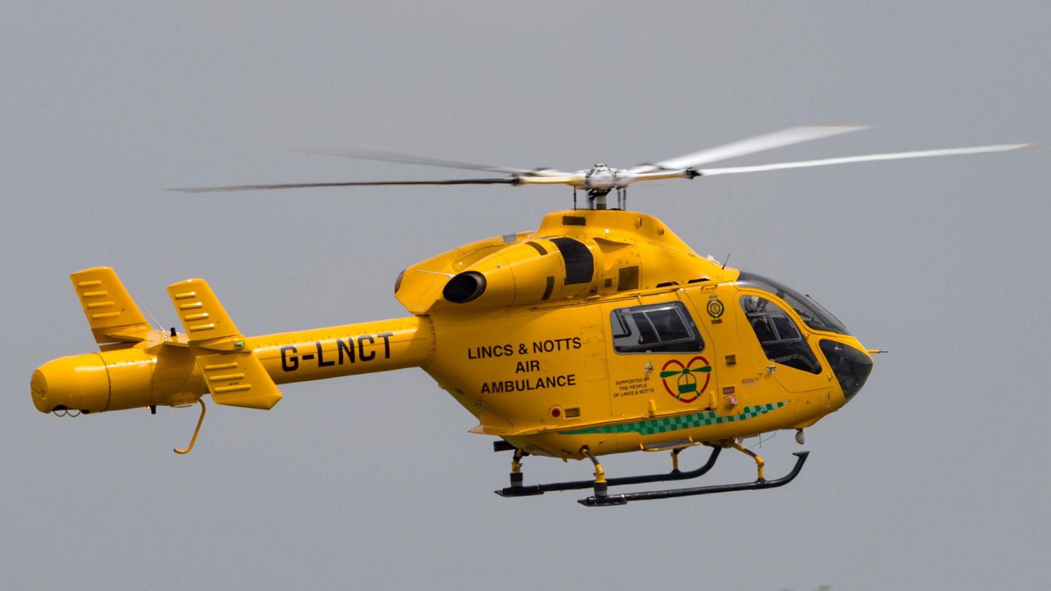 A yellow helicopter in mid flight. The sky is grey