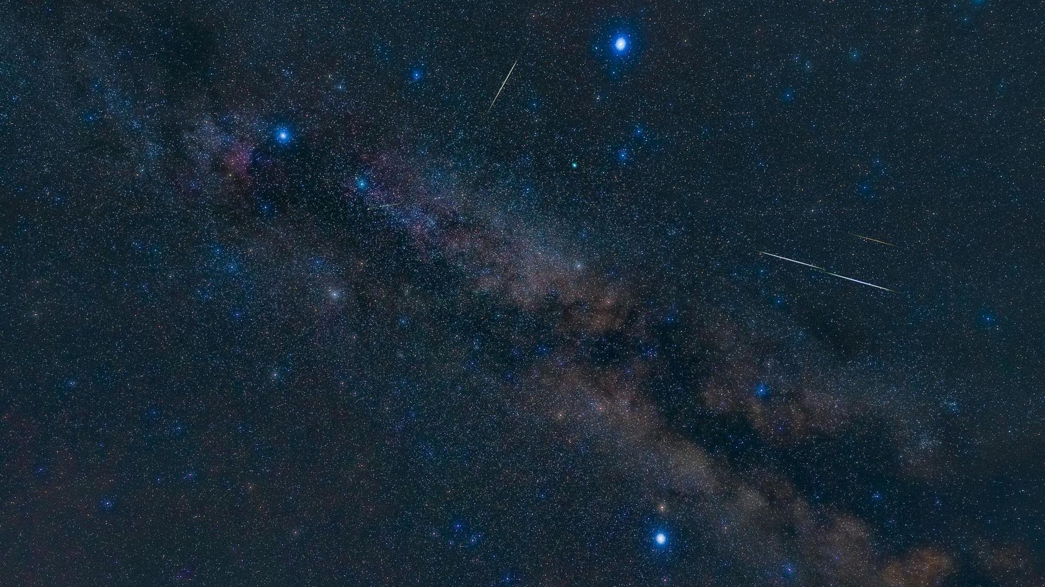 Dark navy blue sky with three bright stars arranged in a triangle shape and meteor streaks flashing across the sky