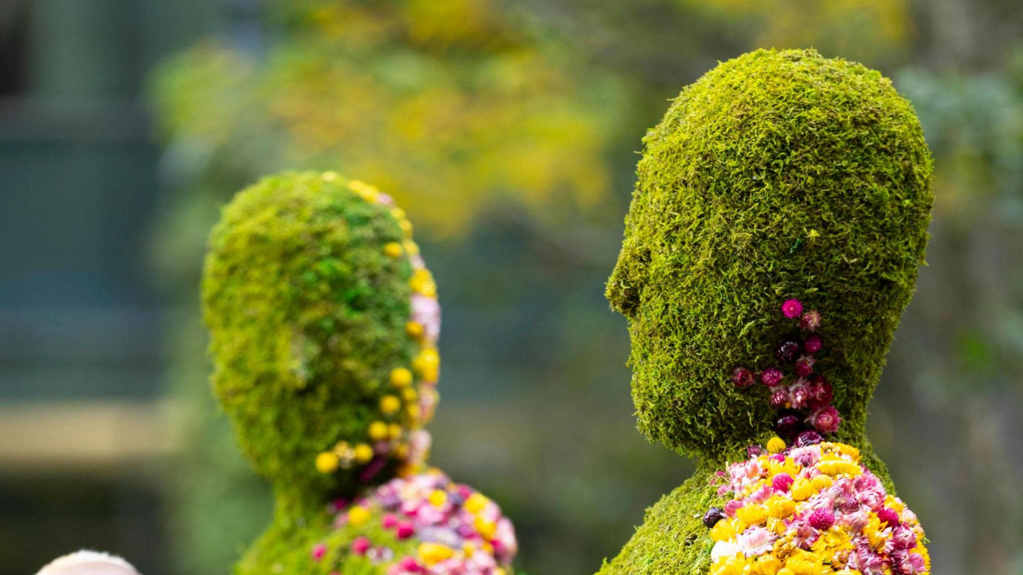 The heads of two figures, larger than life size, one male and one female, made out of moss.