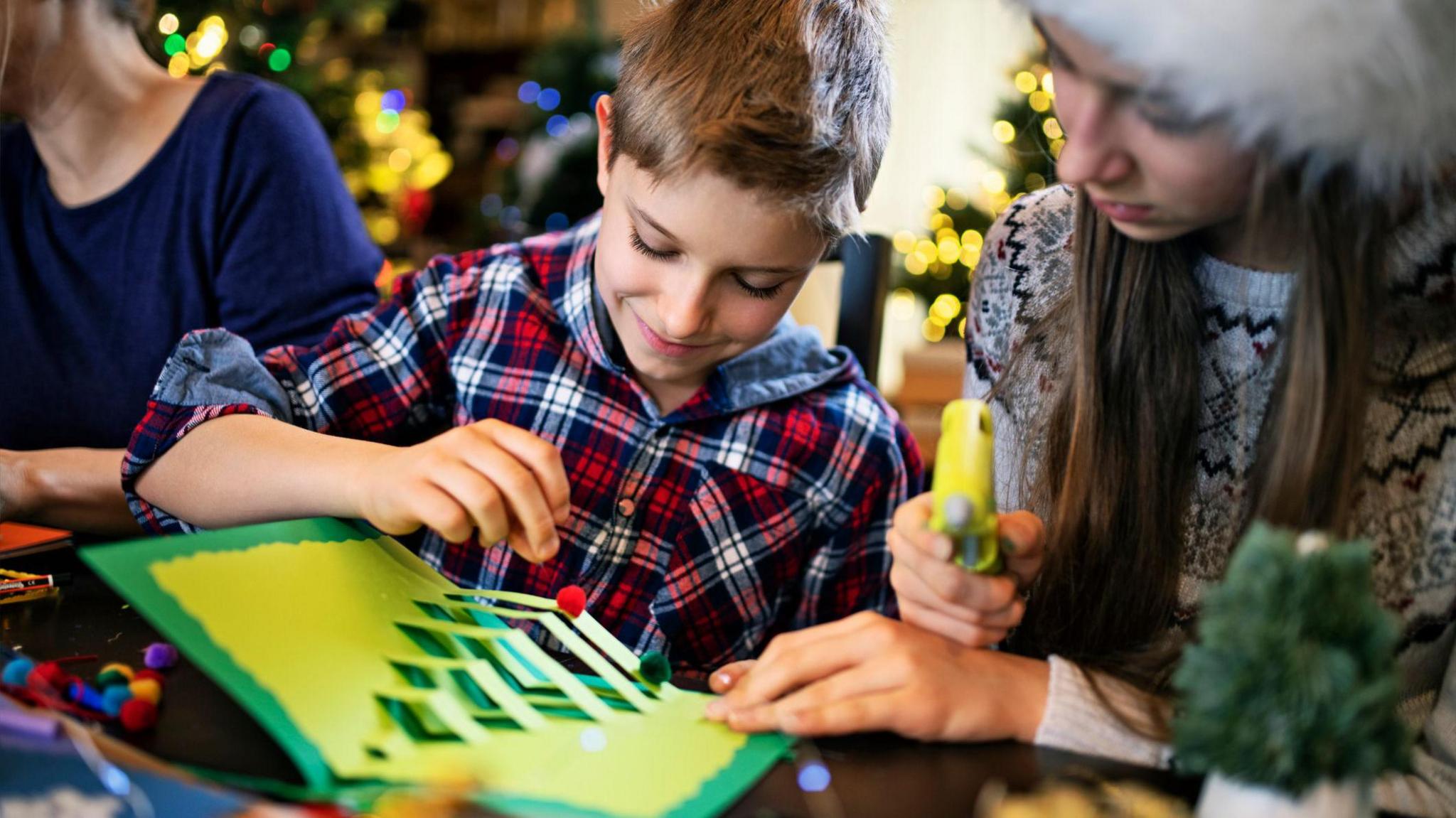 A child makes a Christmas card at home with siblings.