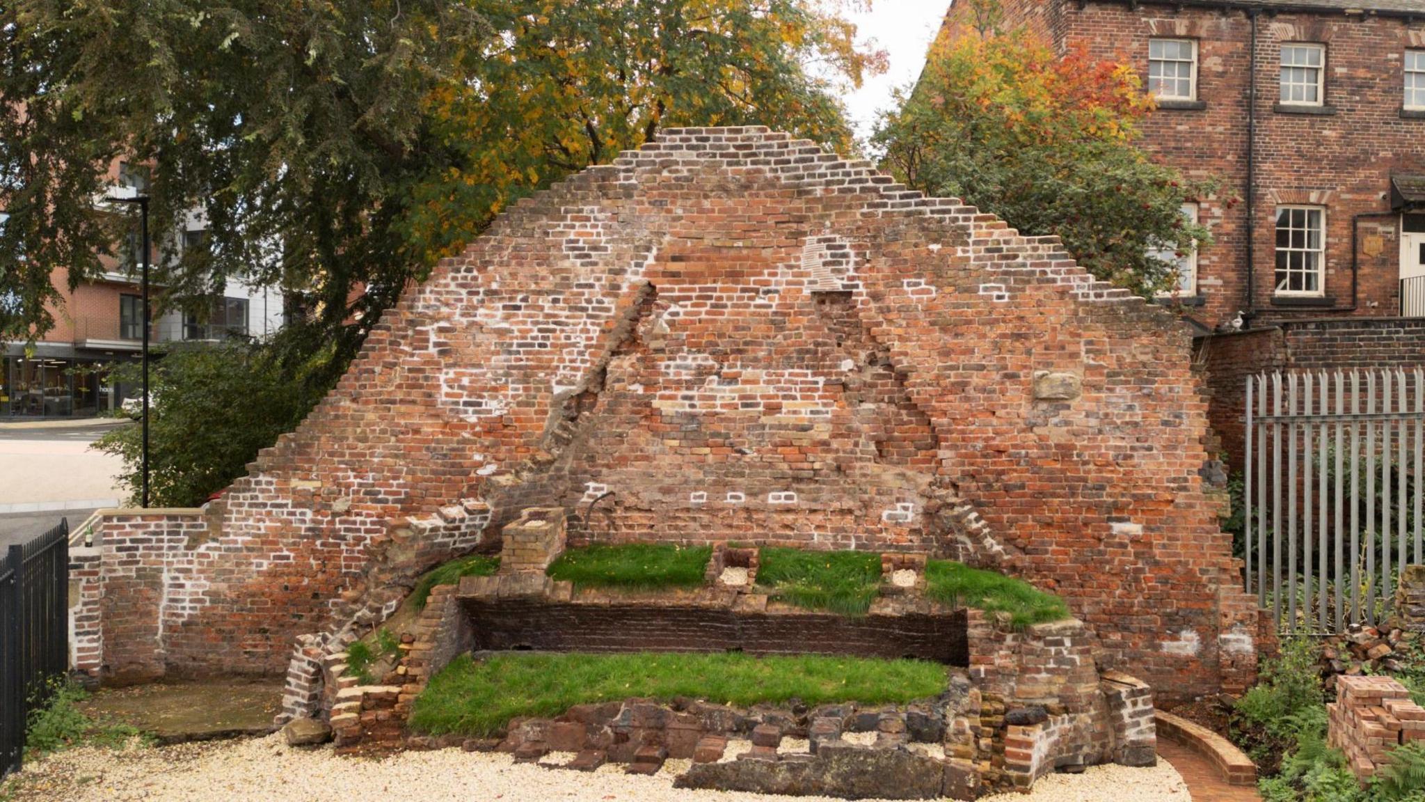 Remains of two early C19 brick built cementation furnace with parts of the cone shaped super structures incorporated into a boundary wall.