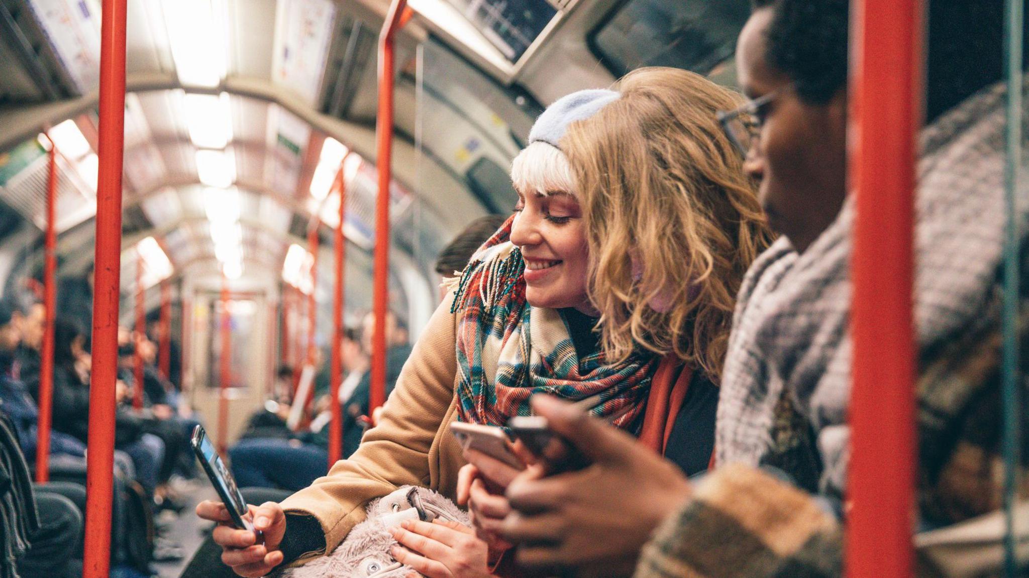 A group of friends look at phones whilst travelling on the tube