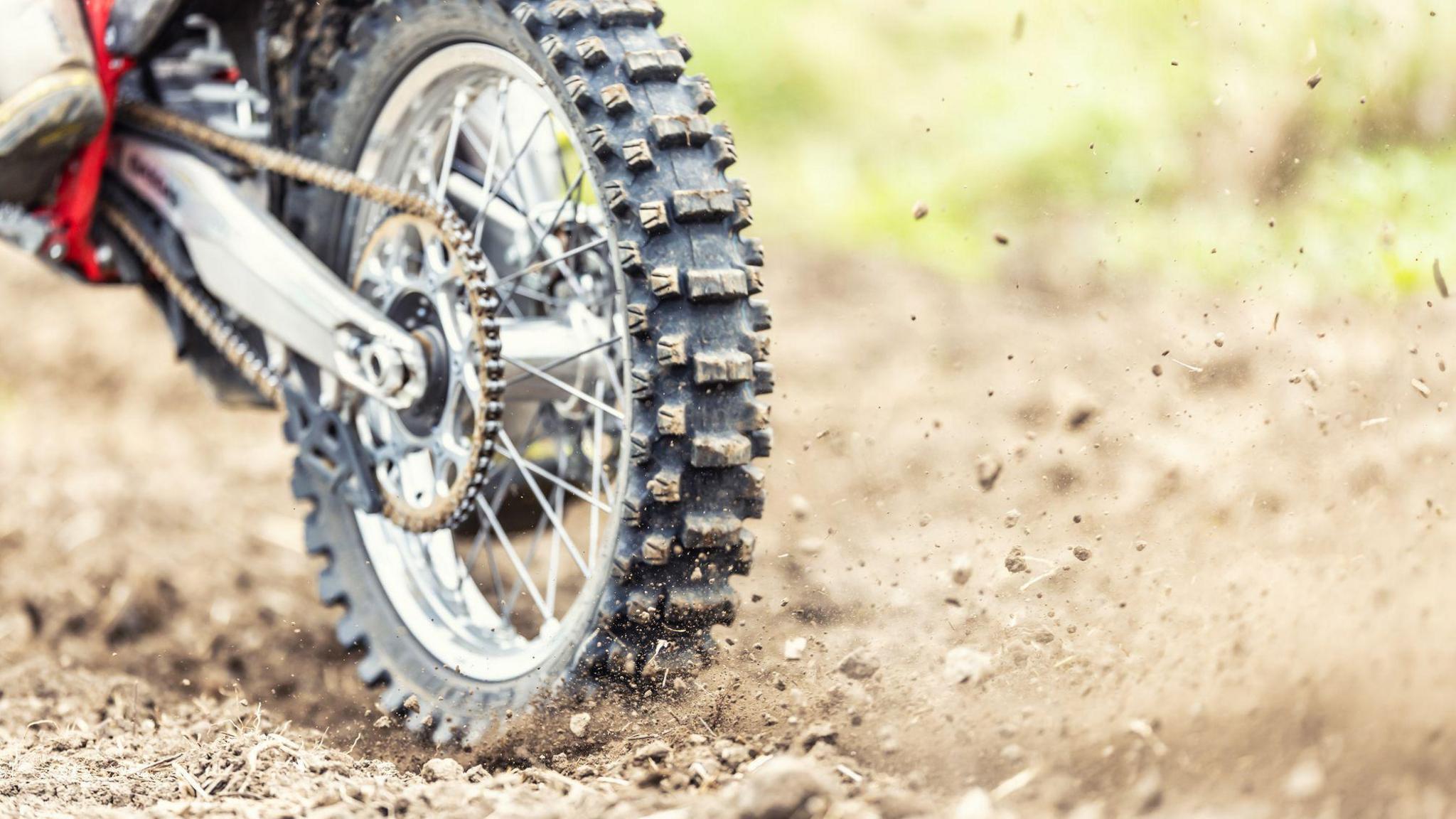 A red scrambler bike's back wheel. It is kicking up some muck. 