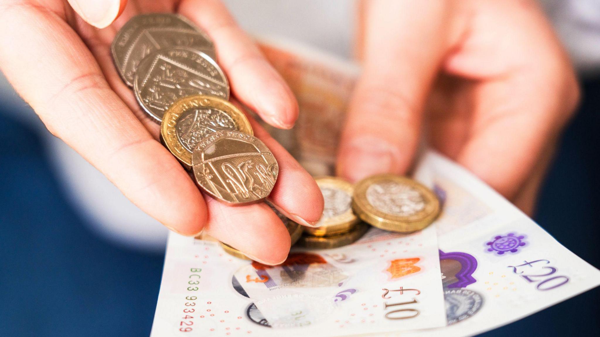 A hand holding coins and a 10 and 20 GBP note.