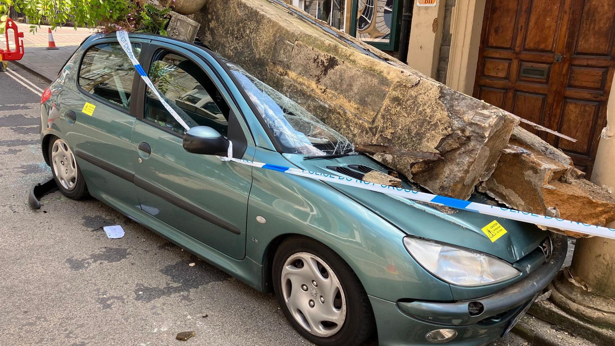 Car with police tape around and large stone on top