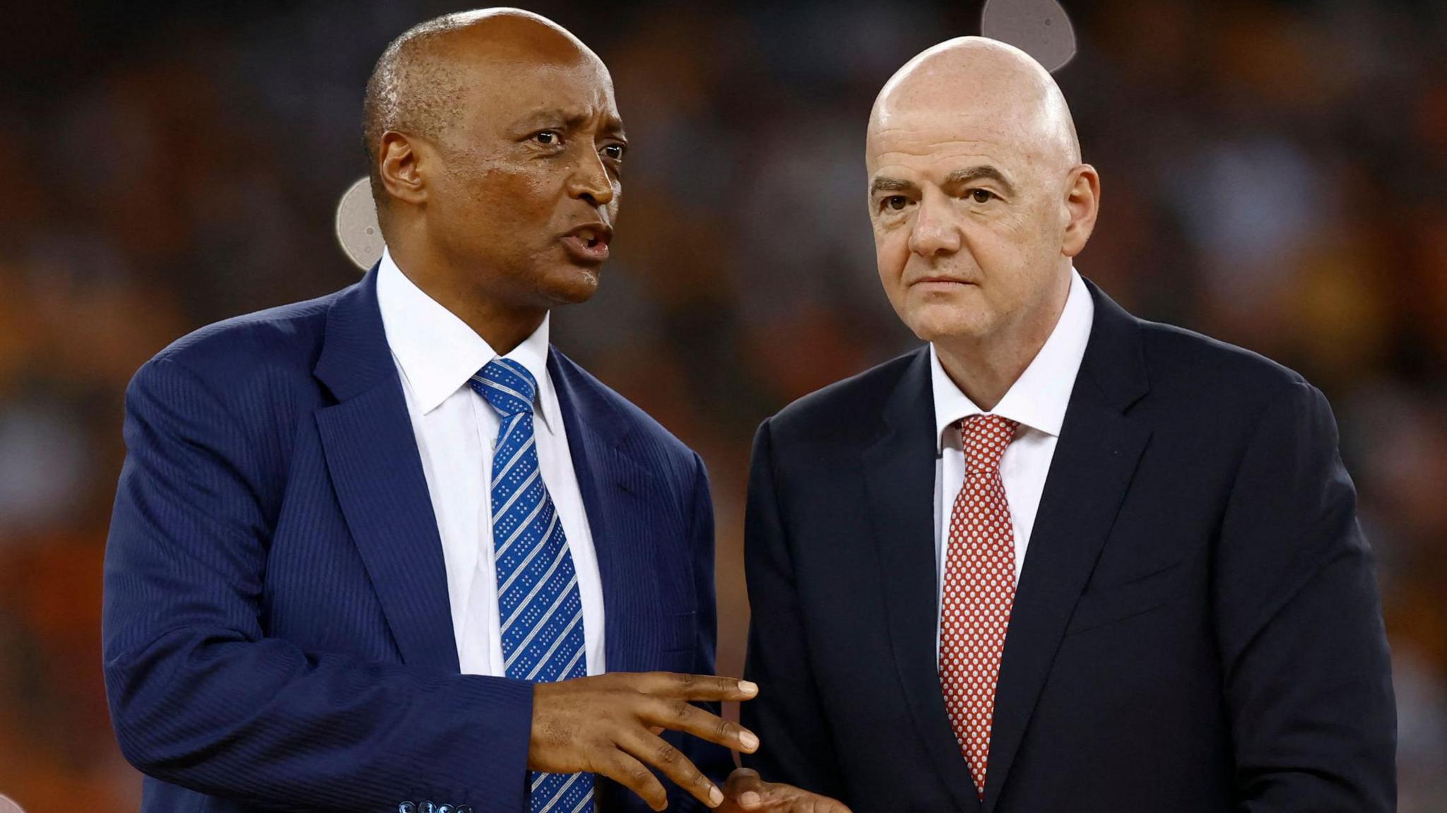 Patrice Motsepe and Gianni Infantino, both wearing suit and tie, talk closely, with Infantino listening to Motsepe