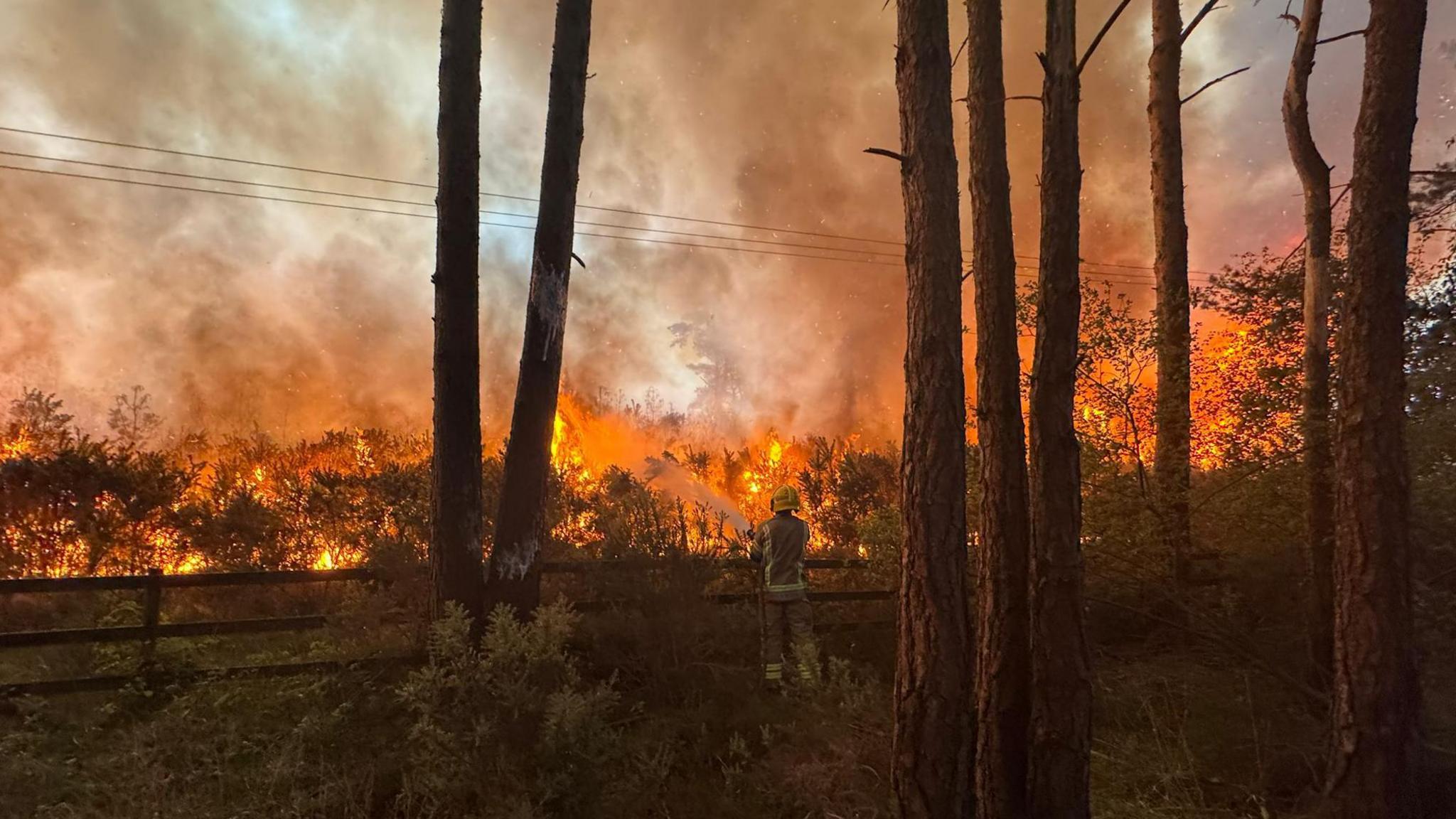 A firefighters sprays the heath fire from his fire hose, as thick plumes of smoke fill the sky.