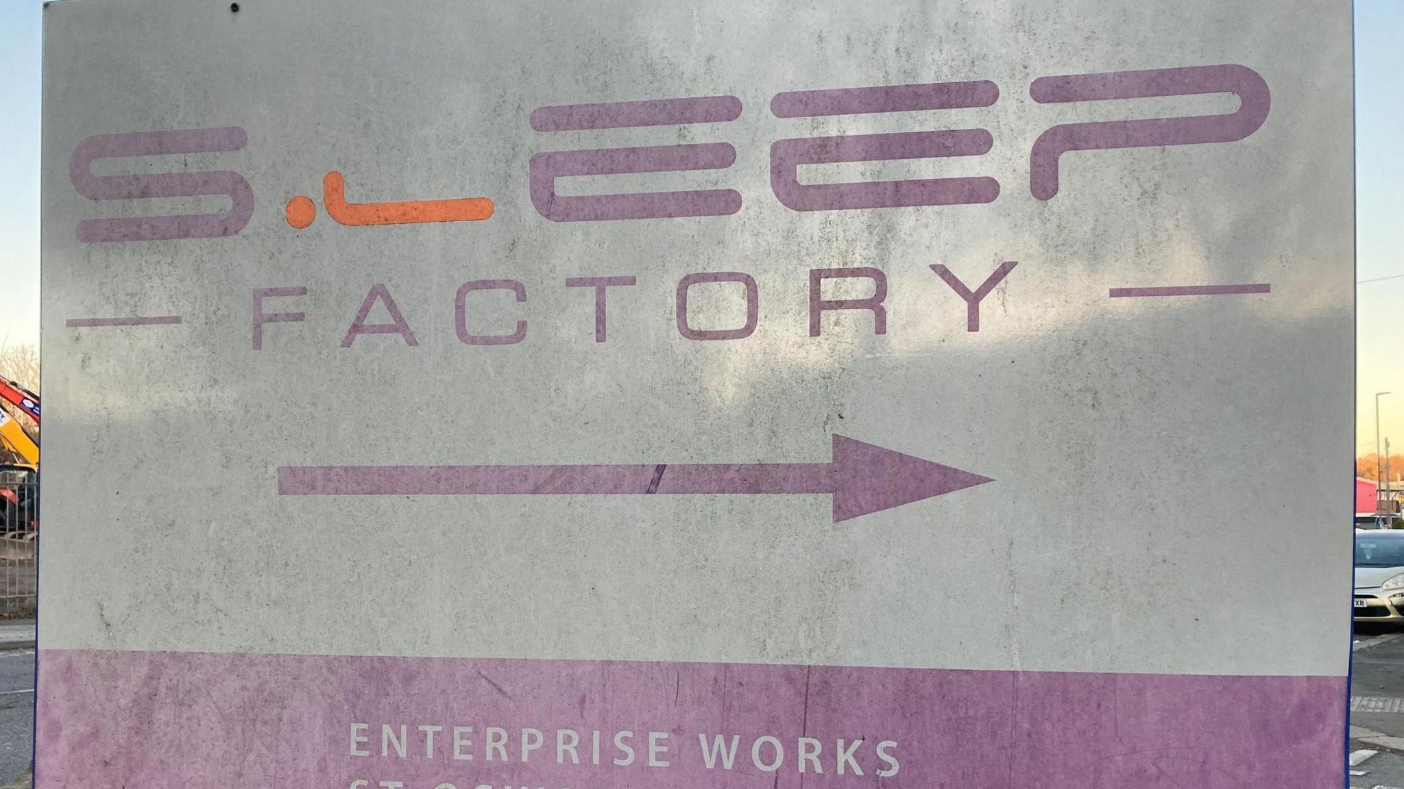 A close-up of a sign which reads, in purple letters 'Sleep Factory'. An arrow pointing to the right is underneath.