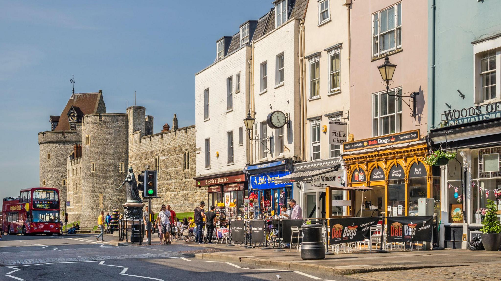 View of Windsor High Street with Queen Victoria statue and the Lower Ward of WindsorCastle with shoppers and pedestrians.