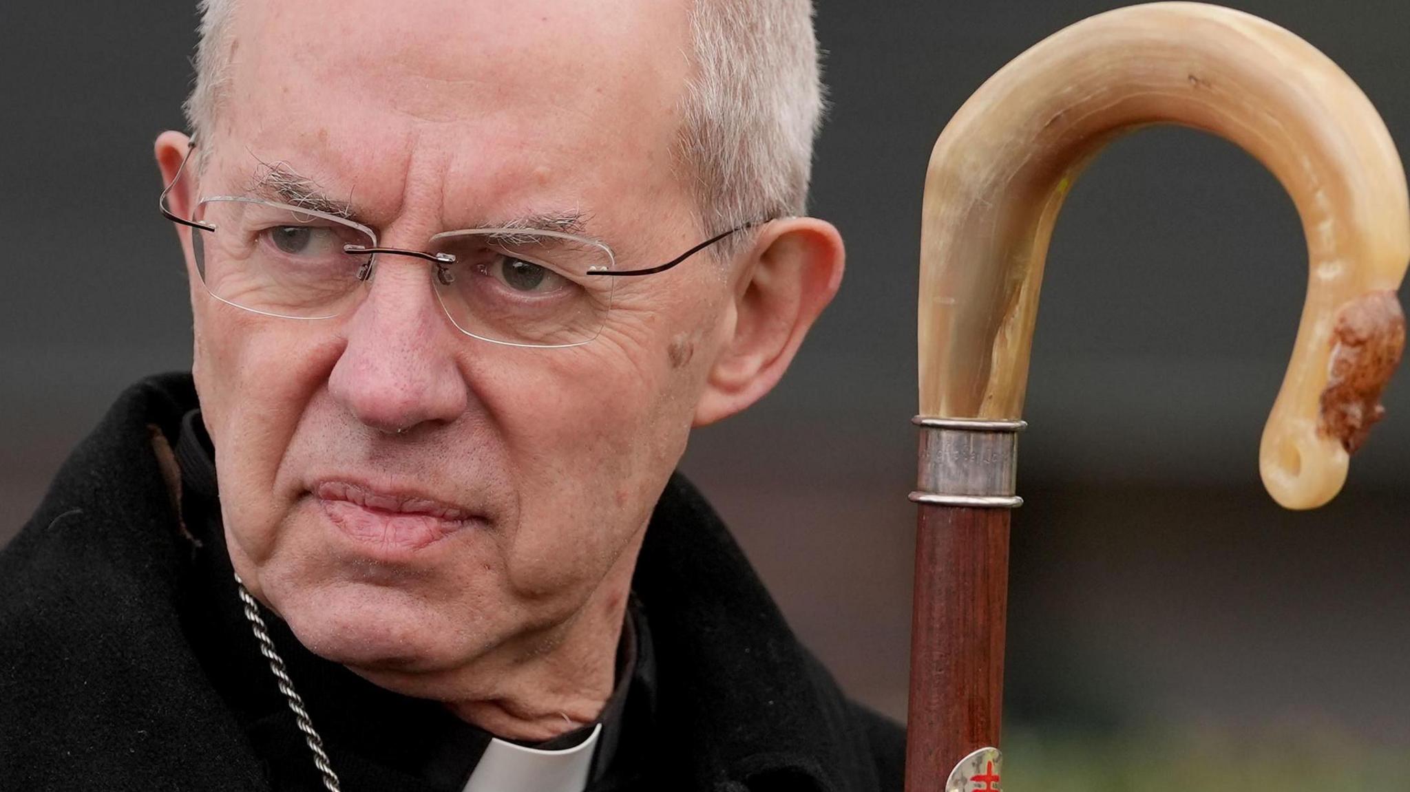 Justin Welby the archbishop of Canterbury looks to the left of frame. He's dressed in a black coat, and is wearing a priests dogcollar. 