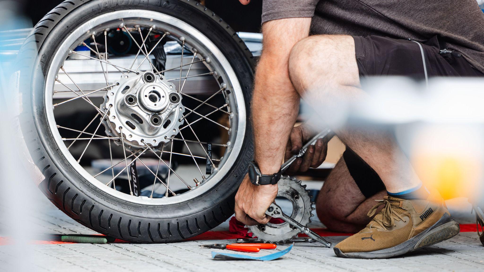 A man kneeling down while working on the wheel of a motorbike with a ratchet.