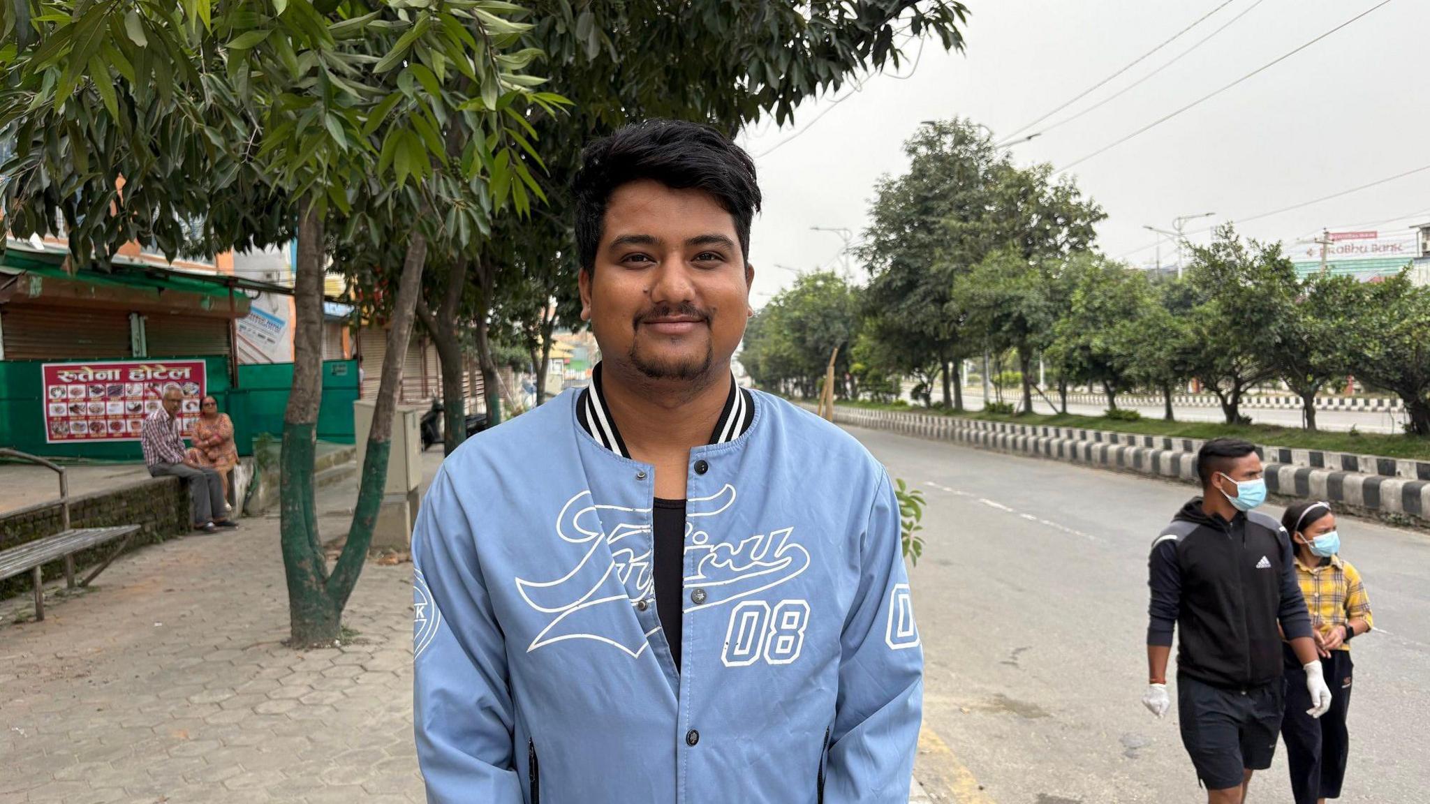 A man standing in a blue jacket in front of the street 