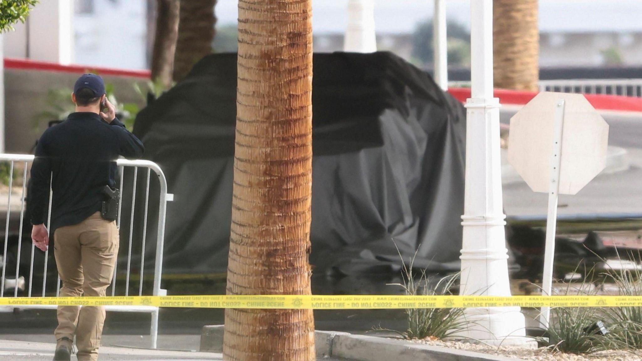 Officer walks near the remains of a black-tarp covered Tesla Cybertruck that burned at the entrance of Trump Tower, in Las Vegas